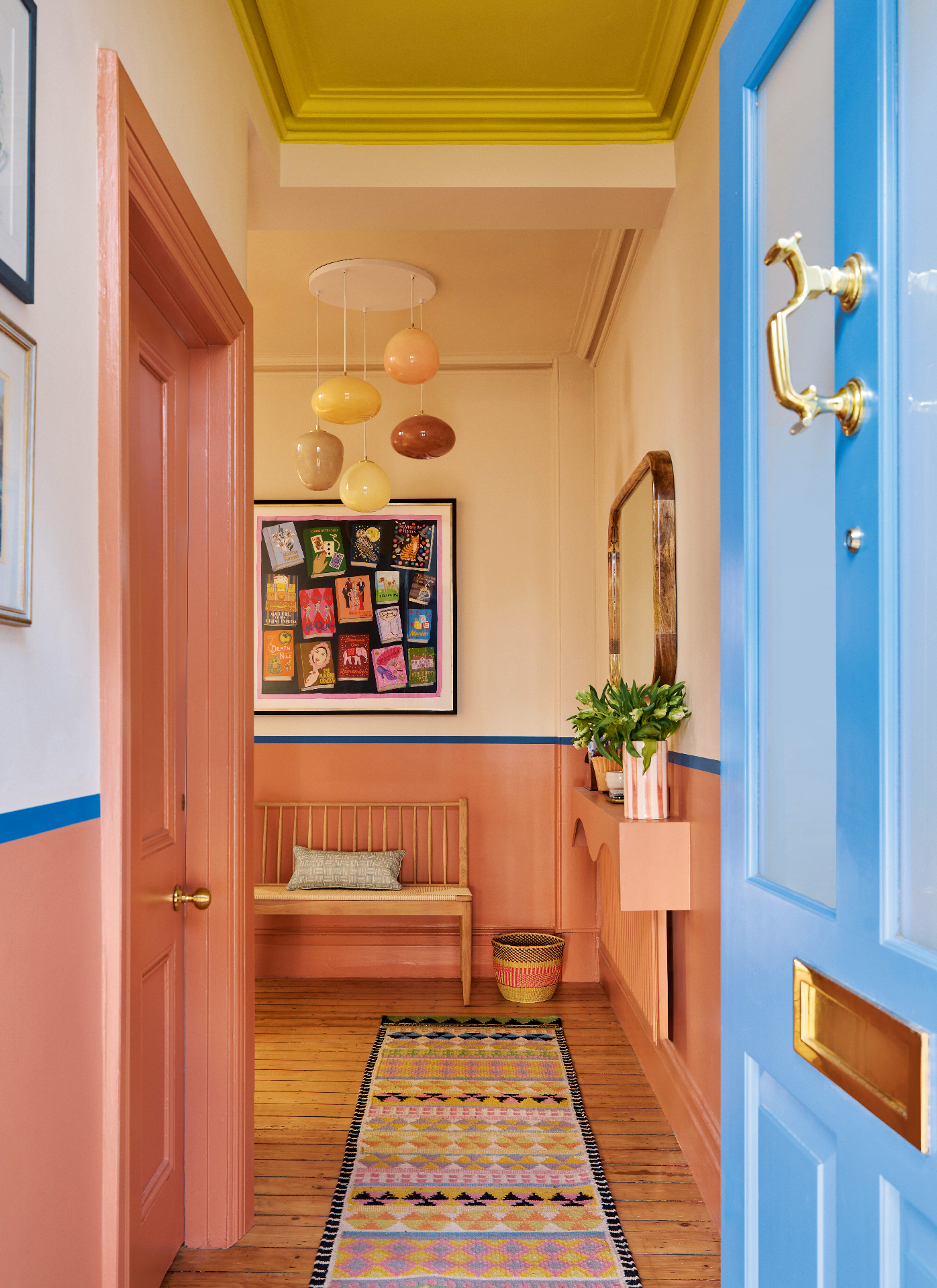 a hallway with a salmon pink door and half wall panelling, a bright blue front door, a patterned runner rug and a bright yellow ceiling