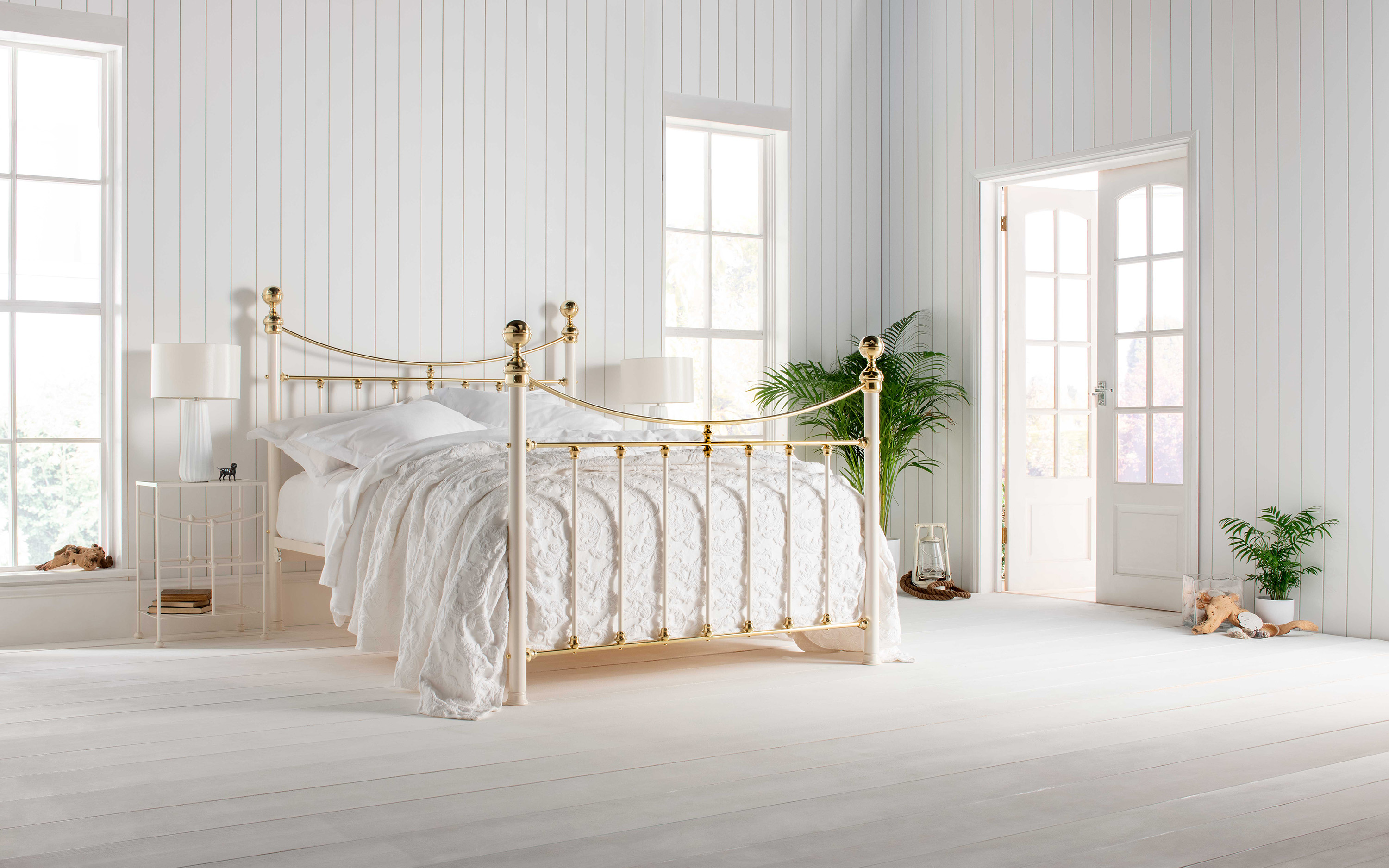 a gold iron bed with white bedding in a white bedroom