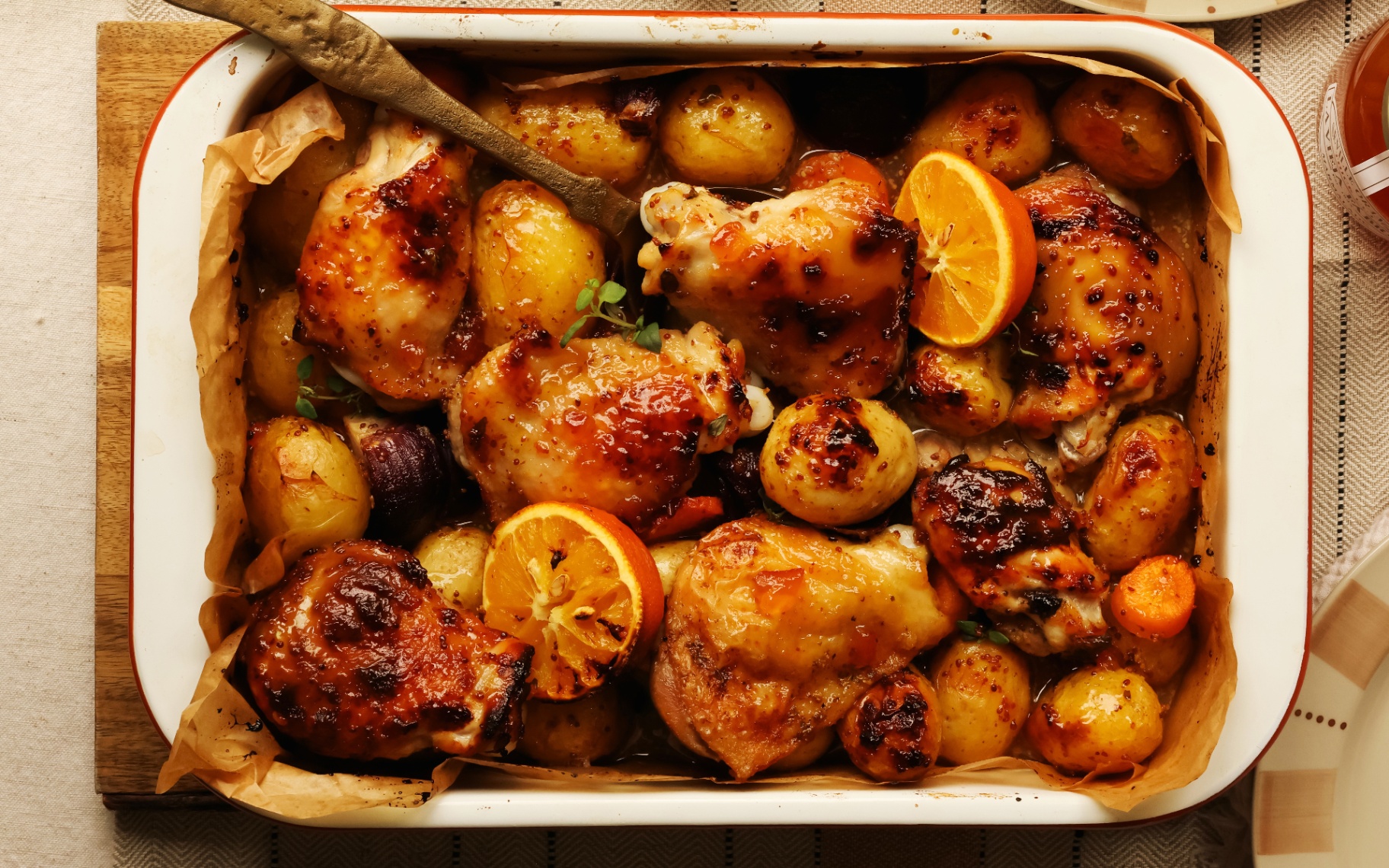 a marmalade chicken traybake in a white enamel roasting tin on a wooden table