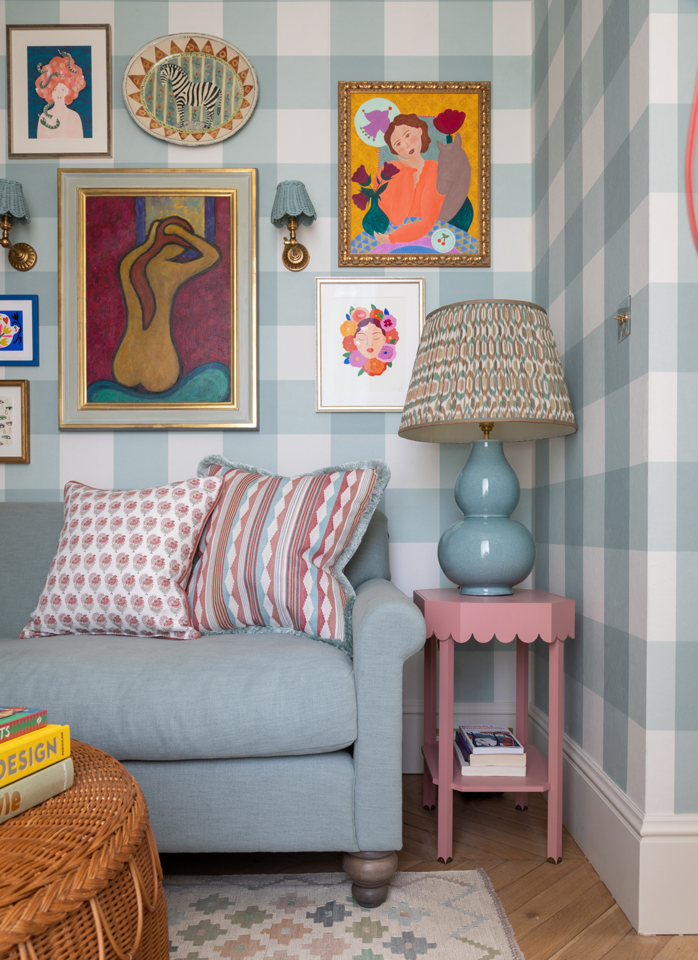 a living room corner with blue and white gingham wallpaper, a blue sofa, a slim pink scalloped side table and a gallery wall