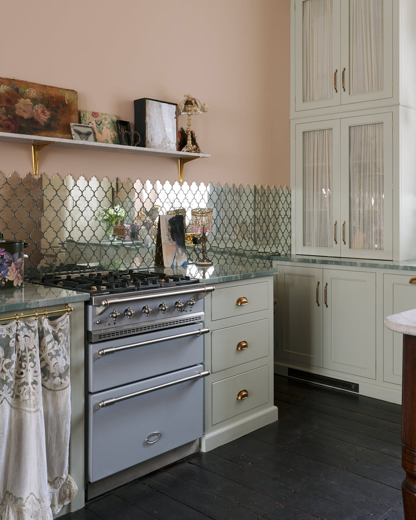 a kitchen withmirroedtile splashback, a pale blue range cooker, plaster pink walls and a large white cabinet