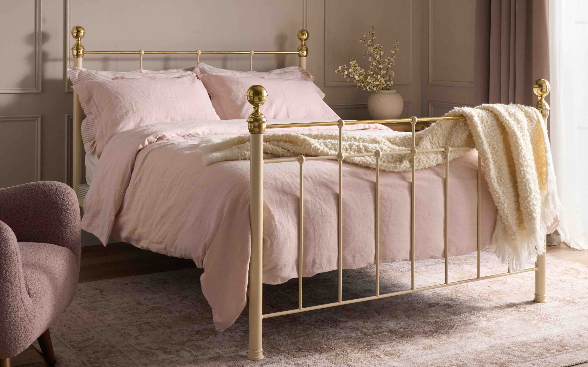 a gold brass bed frame with pink bed sheets and a cream throw over the bed frame