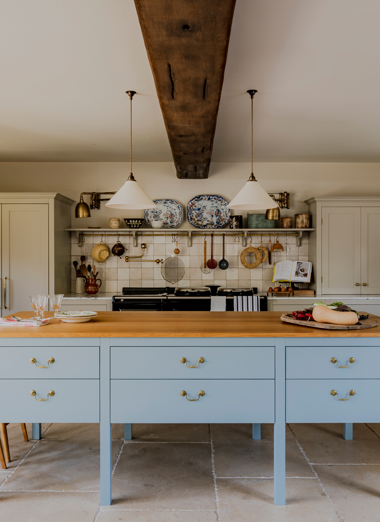 a kitchen with a pale blue kitchen island, two white pendant above it and open shelves on the back wall with pots and kitchen utensils
