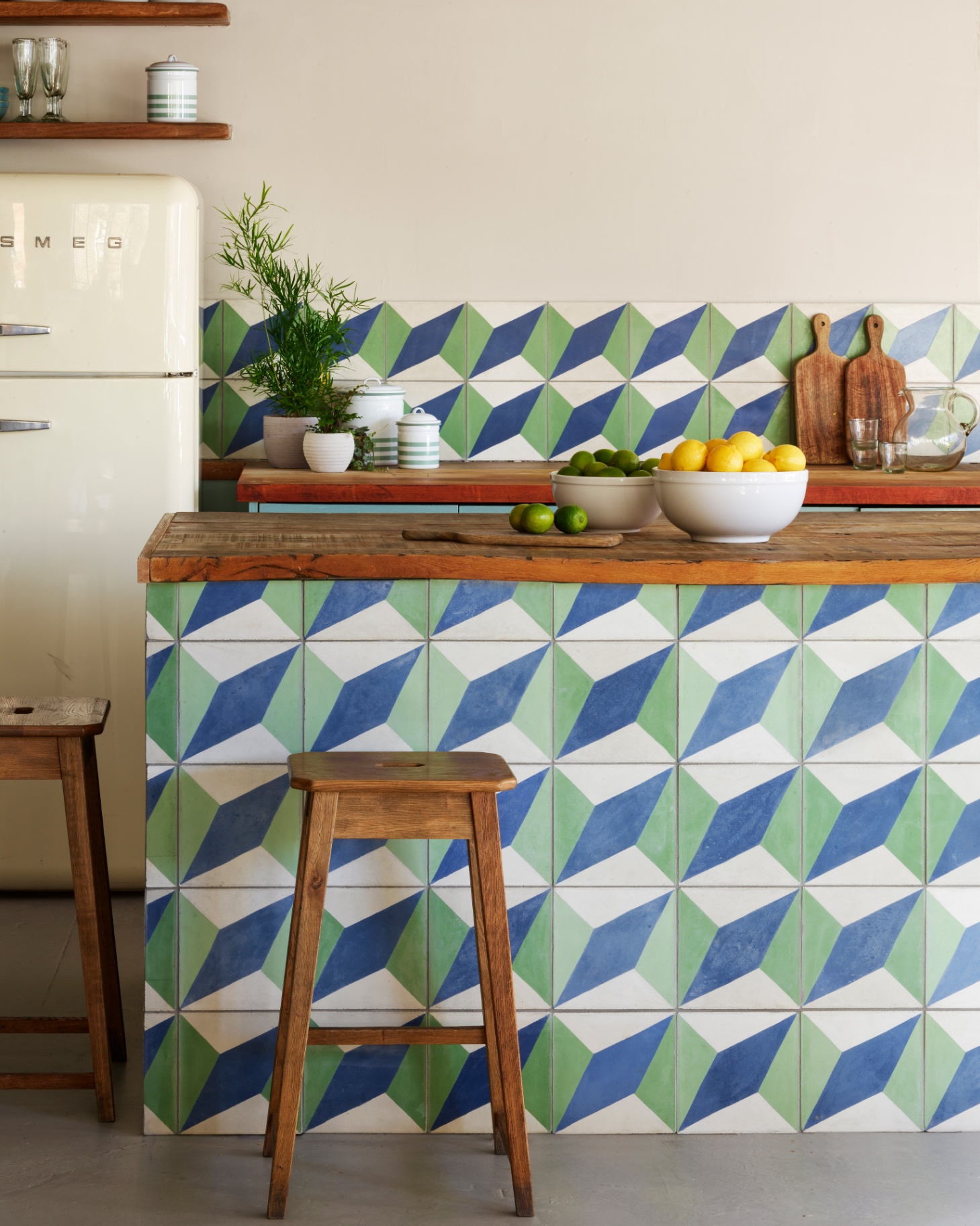 a kitchen with a blue, green and white geometric tile kitchen island with a matching splashback and a white smeg fridge