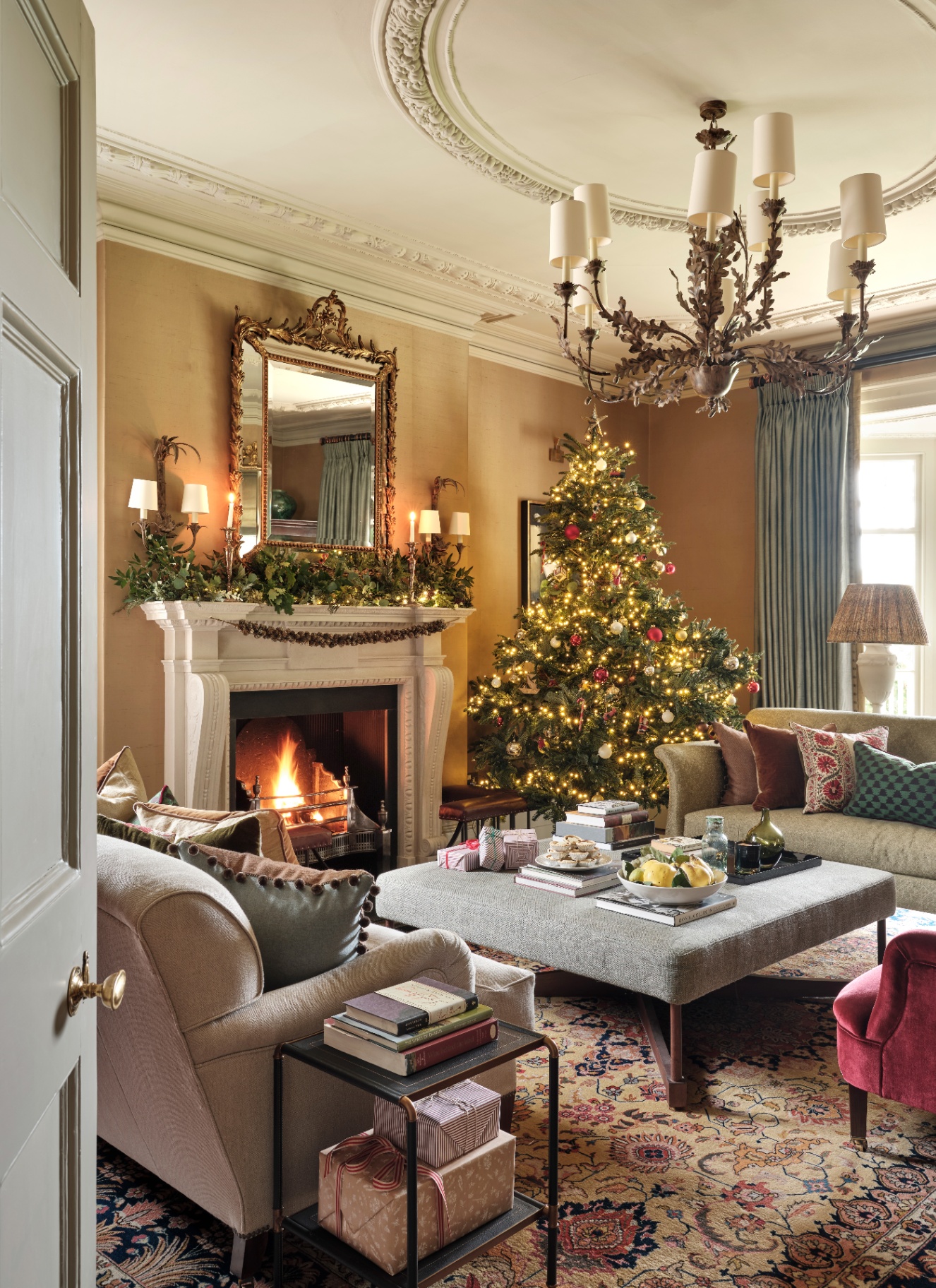 A cozy living room with a glowing Christmas tree in the corner, a roaring fireplace with a garland, and plush velvet seating