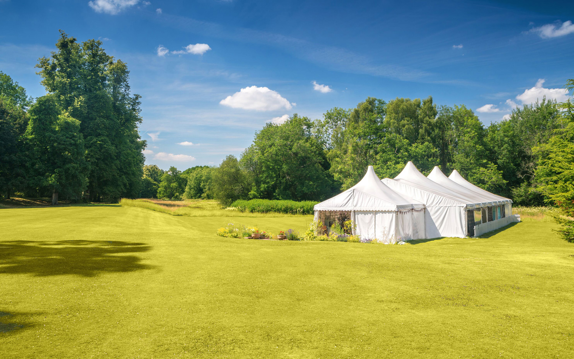 the great british bake off white tent ona green lawn with trees and blue sky in the grounds of welford park