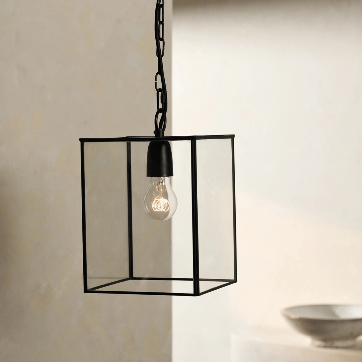a black framed rectangular pendant light with a lit up bulb inside