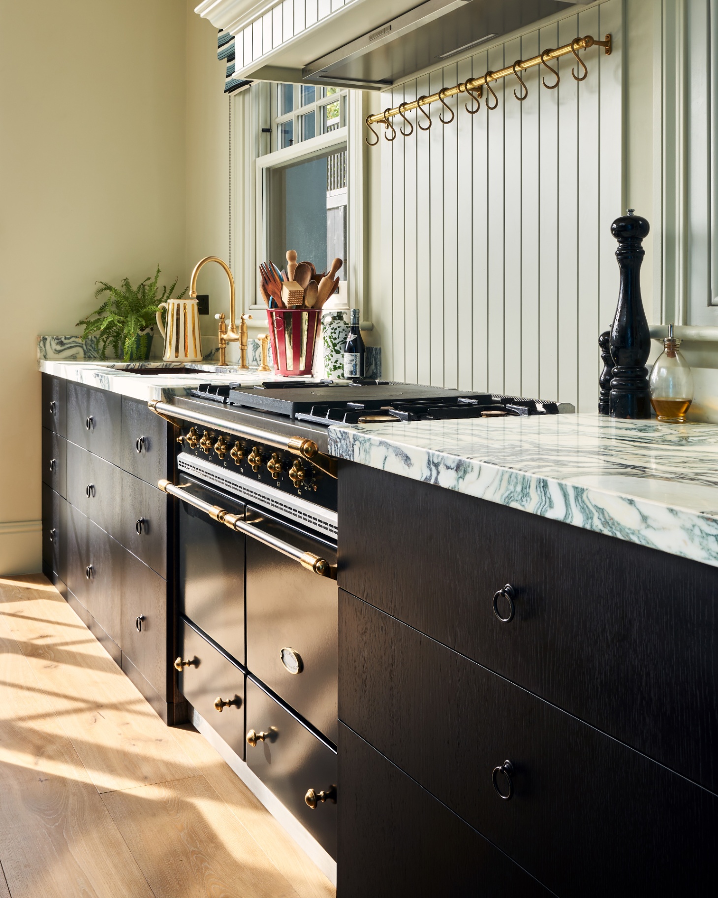 a kitchen with black kitchen cupboards with white marble tops, a large black range cooker and a grey wooden panelled splashback