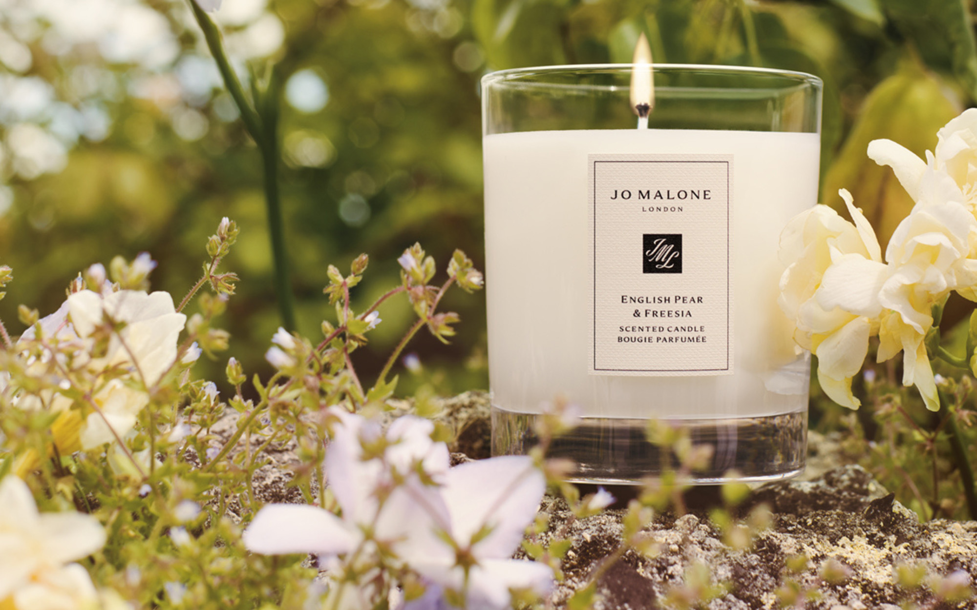 jo malone english pear and freesia candle lit outside surrounded by leaves and blossoms
