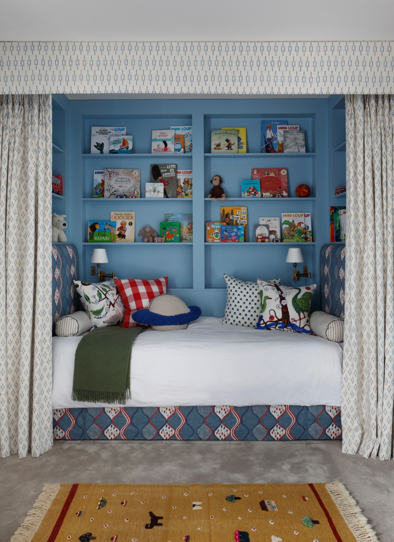 a childrens bedroom with a bed nook behind white patterned curtains and a blue painted wall behind the bed full of books