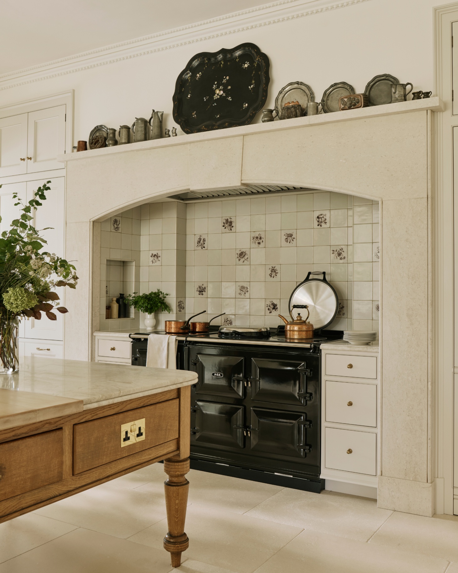 a white country kitchen with a black aga, a white patterned tile splashback behind it and a large farmhouse table