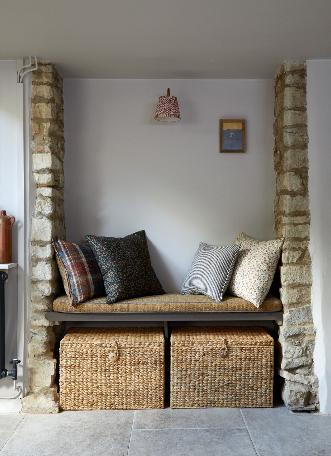 a hallway with white walls, exposed bricks with a built in bench between it and wicker baskets underneath