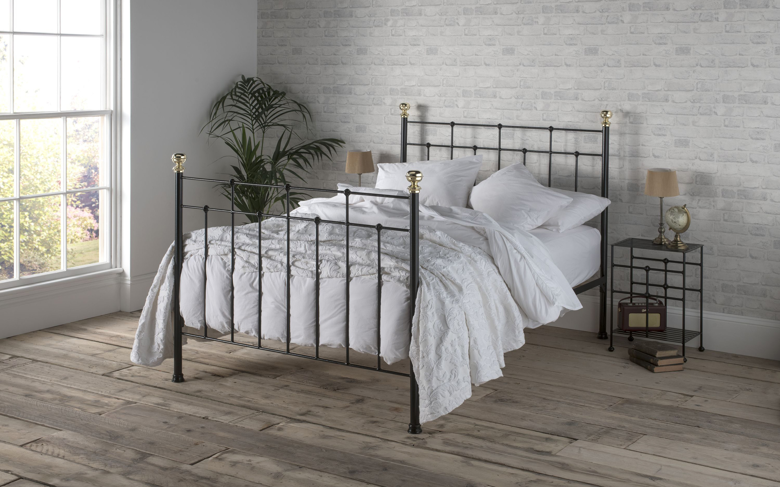 black iron  bed with white bedding in a room with grey brick walls and grey wooden floor