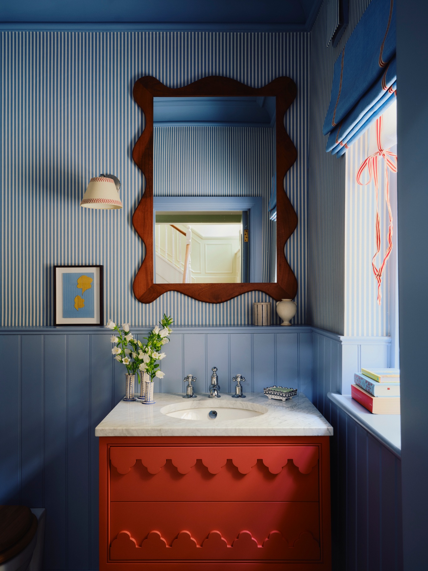 a brightly decorated bathroom pictured with a bright red statement vanity as the focal point with striped wallpaper and wall lights