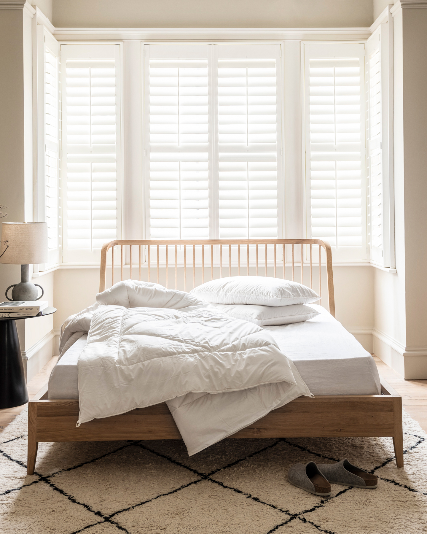 a duvet with no cover on a wooden bed with a cream and black diamond patterned rug under it
