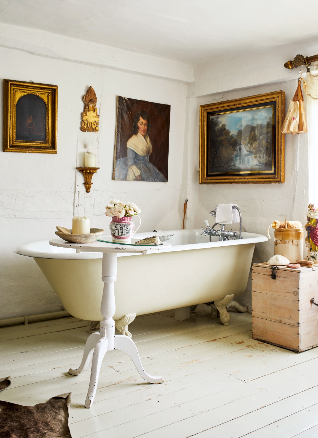 a traditional english bathroom with white painted timber floors, a pale yellow freestanding bath tub and a large paitning in a gold frame