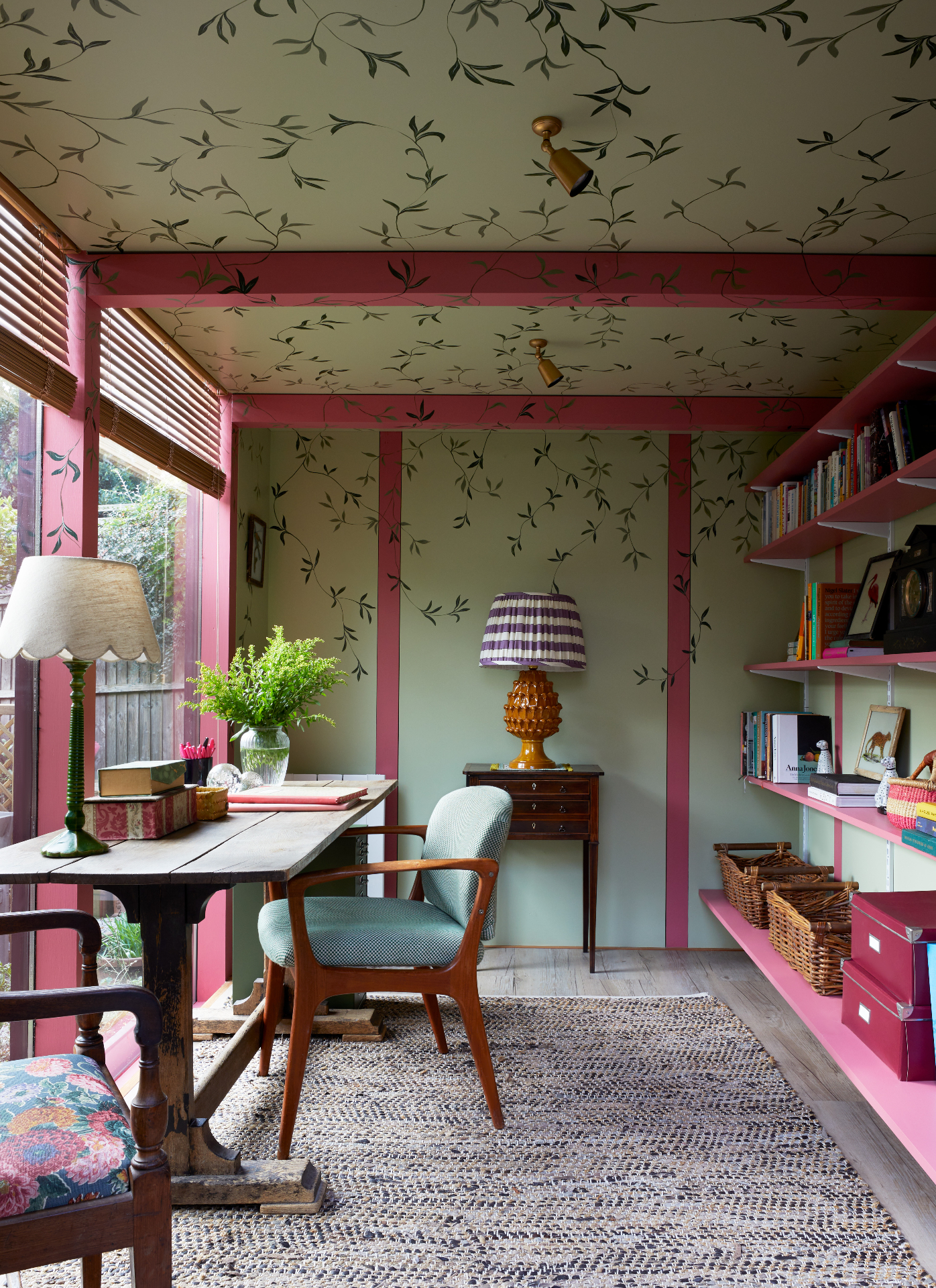 a study with sage green painted walls and ceiling with handpainted trailing ivy, red painted beams and matching shelving and a desk and chair facing the window