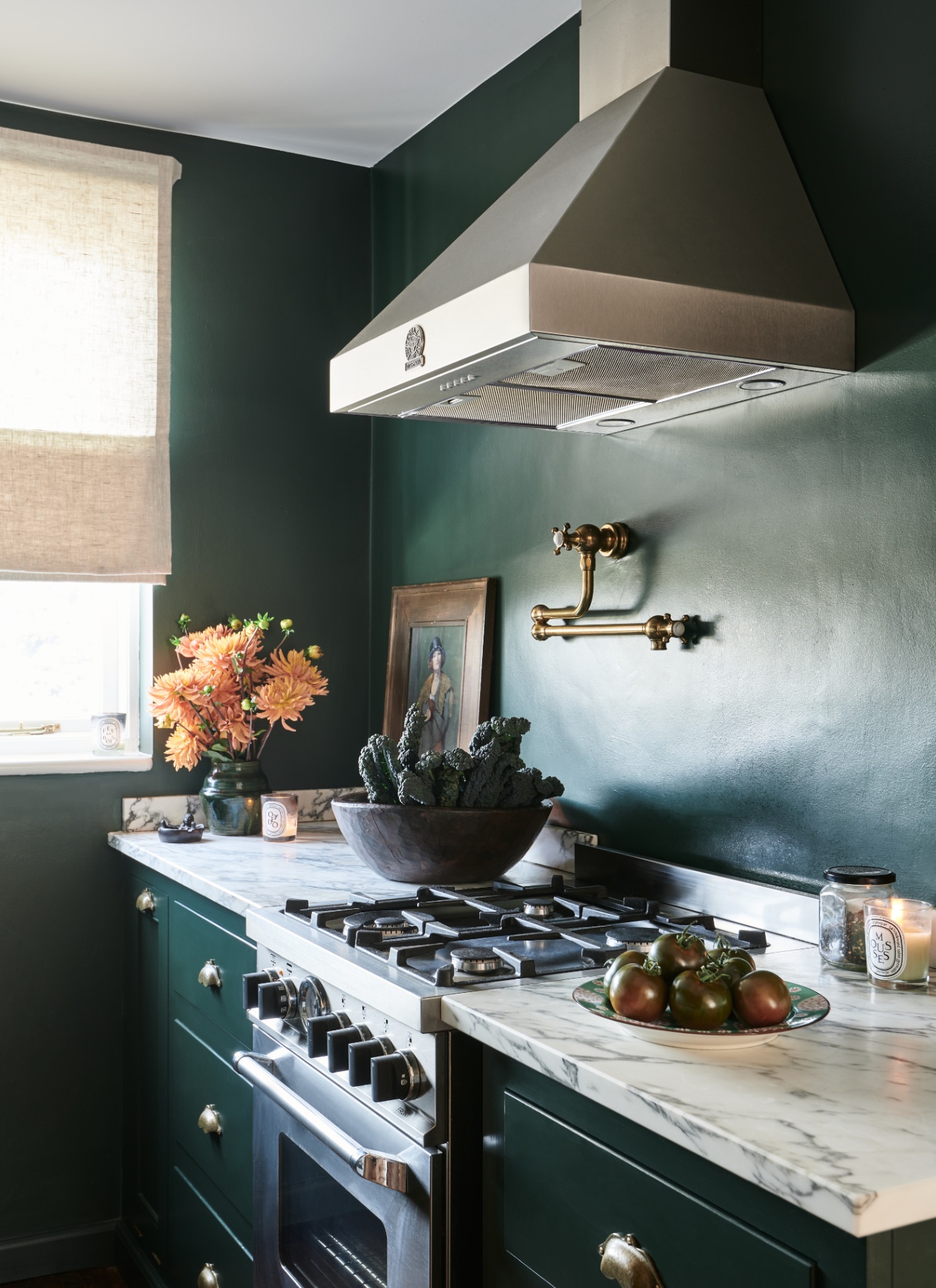 a kitchen with dark green walls, marble counter tops and a large silver extractor hood
