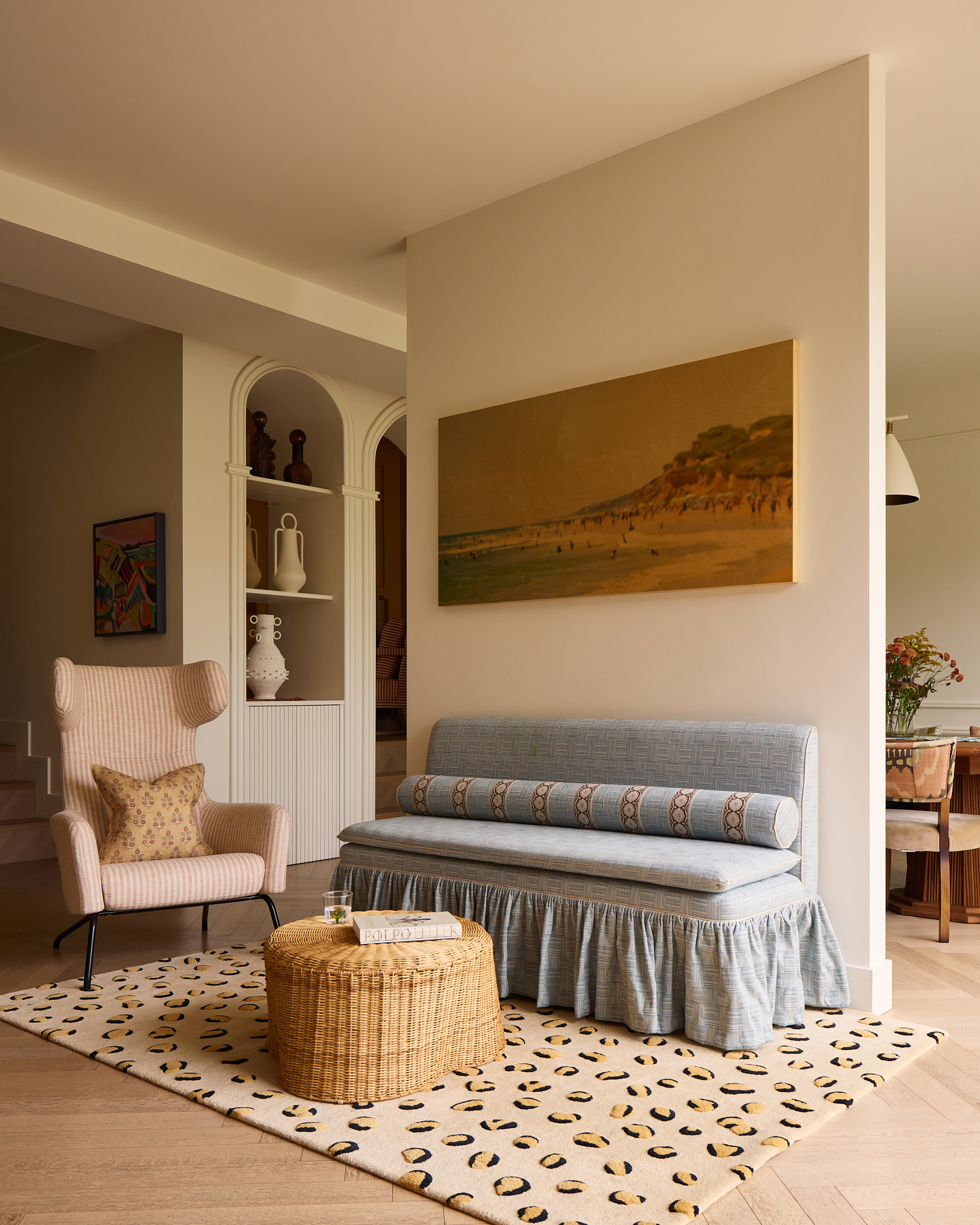 a living room witha pale blue skirted sofa, a leopard print rug and a wicker coffee table