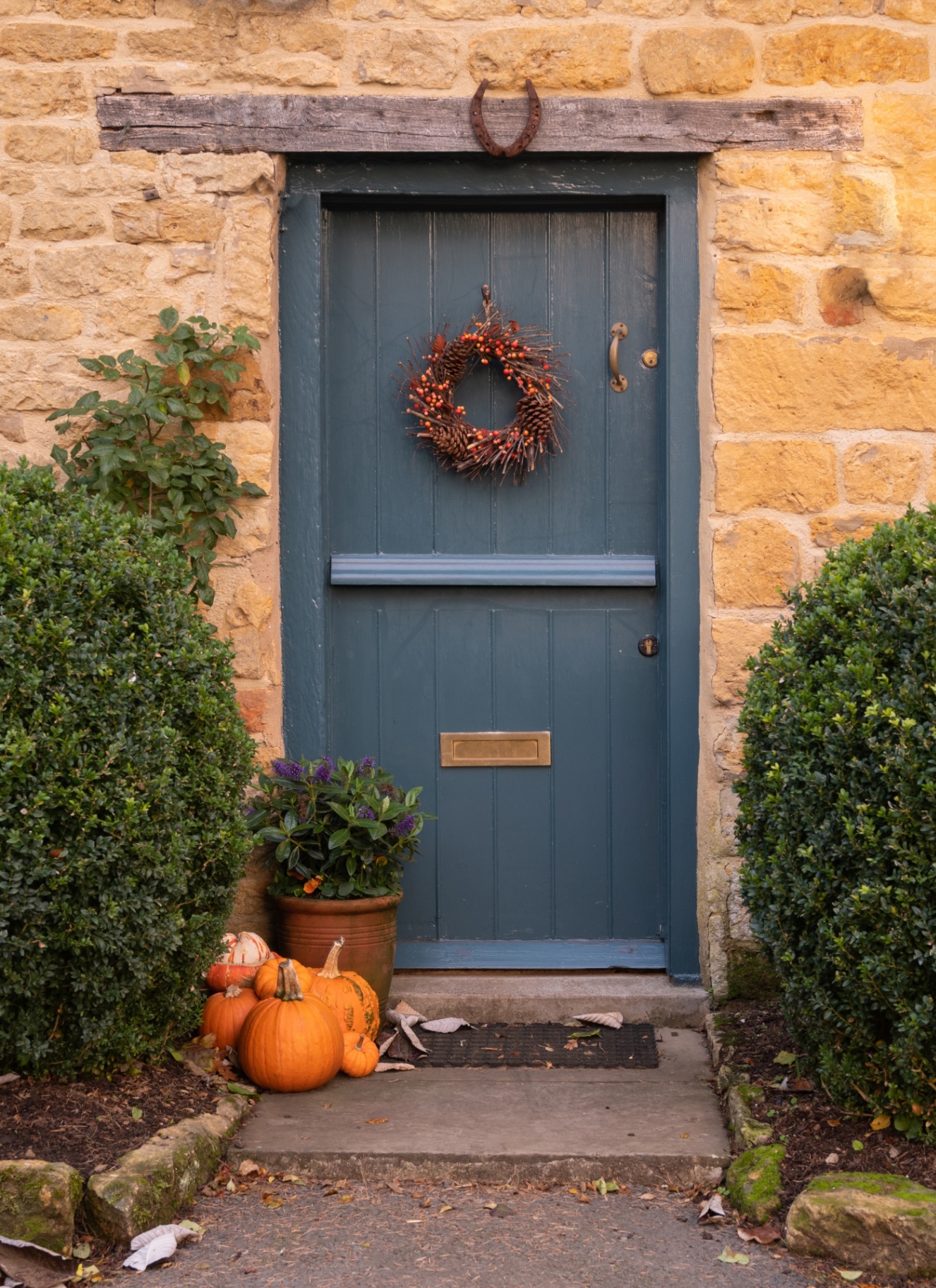 a cotswold stone house with a blue door and an autumn wreath and a collection of pumpkins on the floor