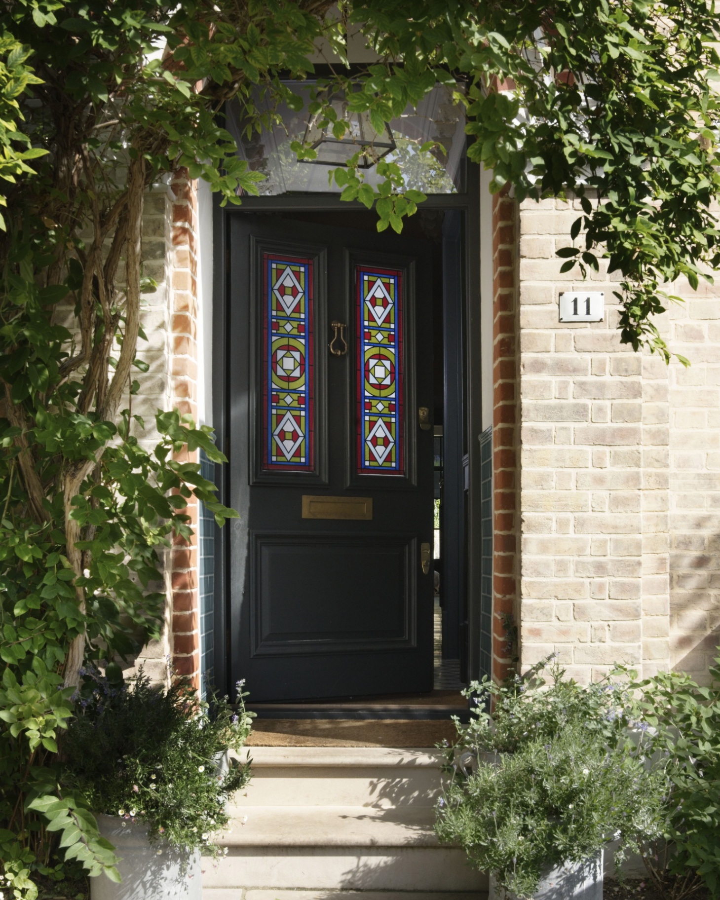 a dark green front door with a colourful glass film on the panels, a porch with a black lantern and greenery arching over the porch