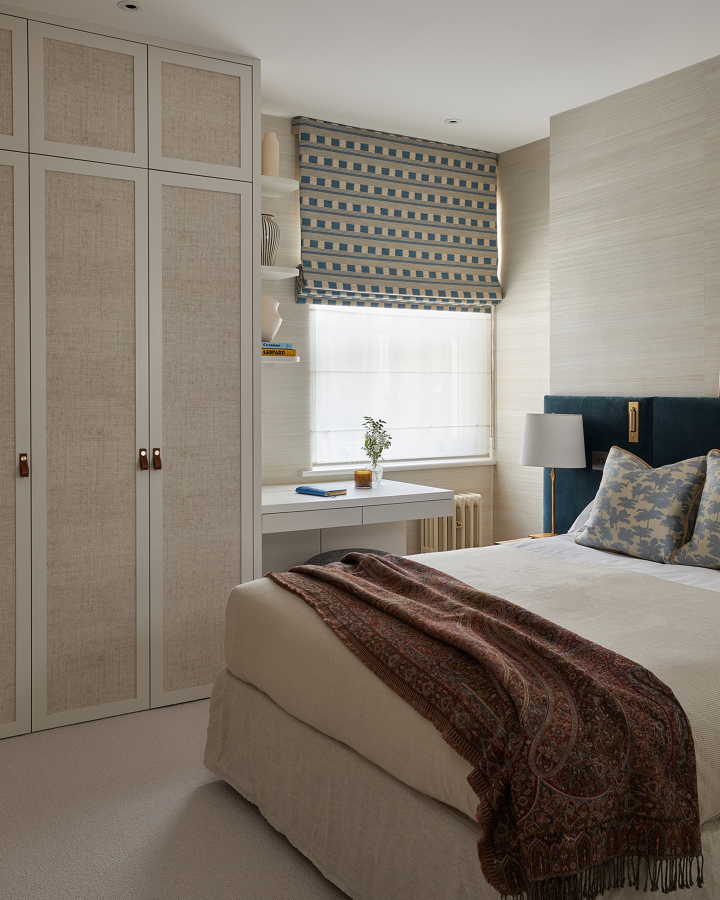 a bedroom with white walls, a bed with white bedding and a dark red patterned throw on the end and a large neutral built in wardrobe