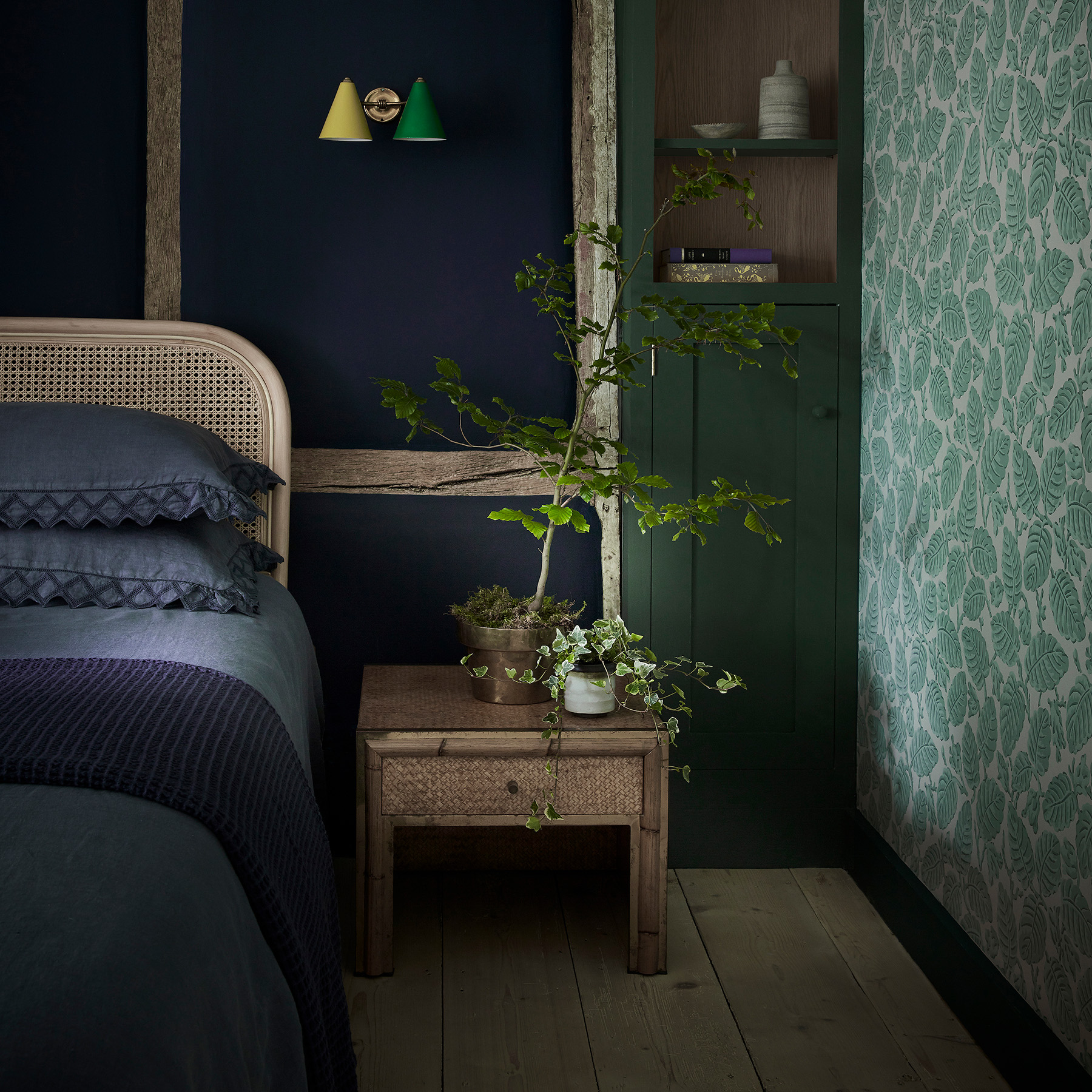 a dark green bedroom witha wooden bedside table and botanical wallpaper