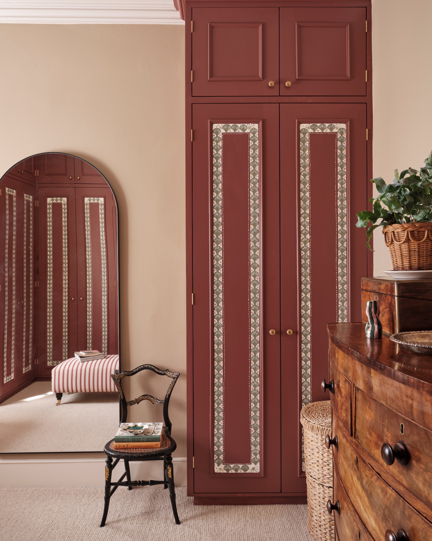 a dressing room with a tall dark red painted warbrobe with white border detail and a tall arched mirror leaning against the wall