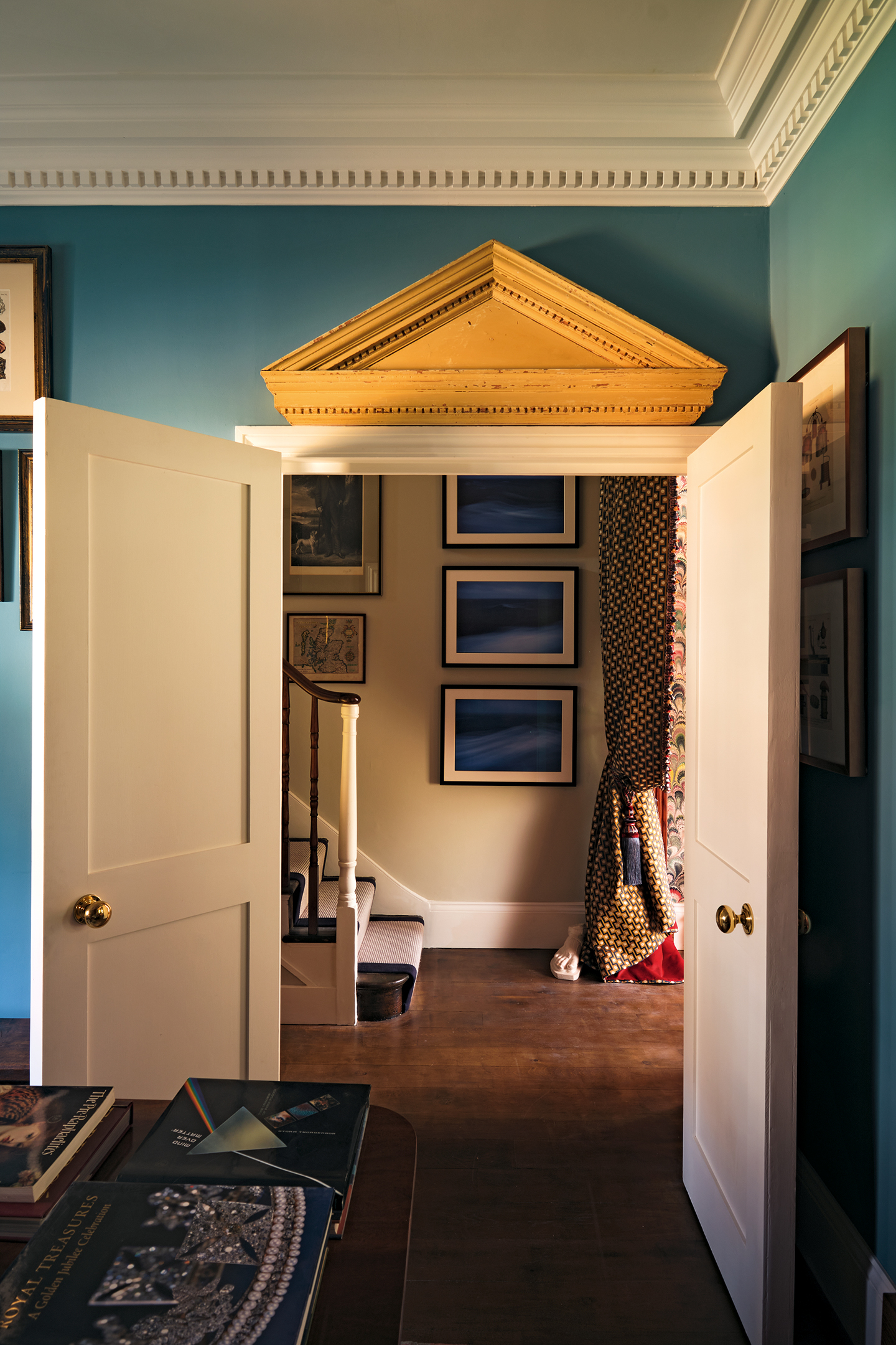 a large double internal door in a townhouse, looking through to the hall and stairs. A large classic pediment sits above the doorway against deep blue walls. Decorative coving lines the wall above