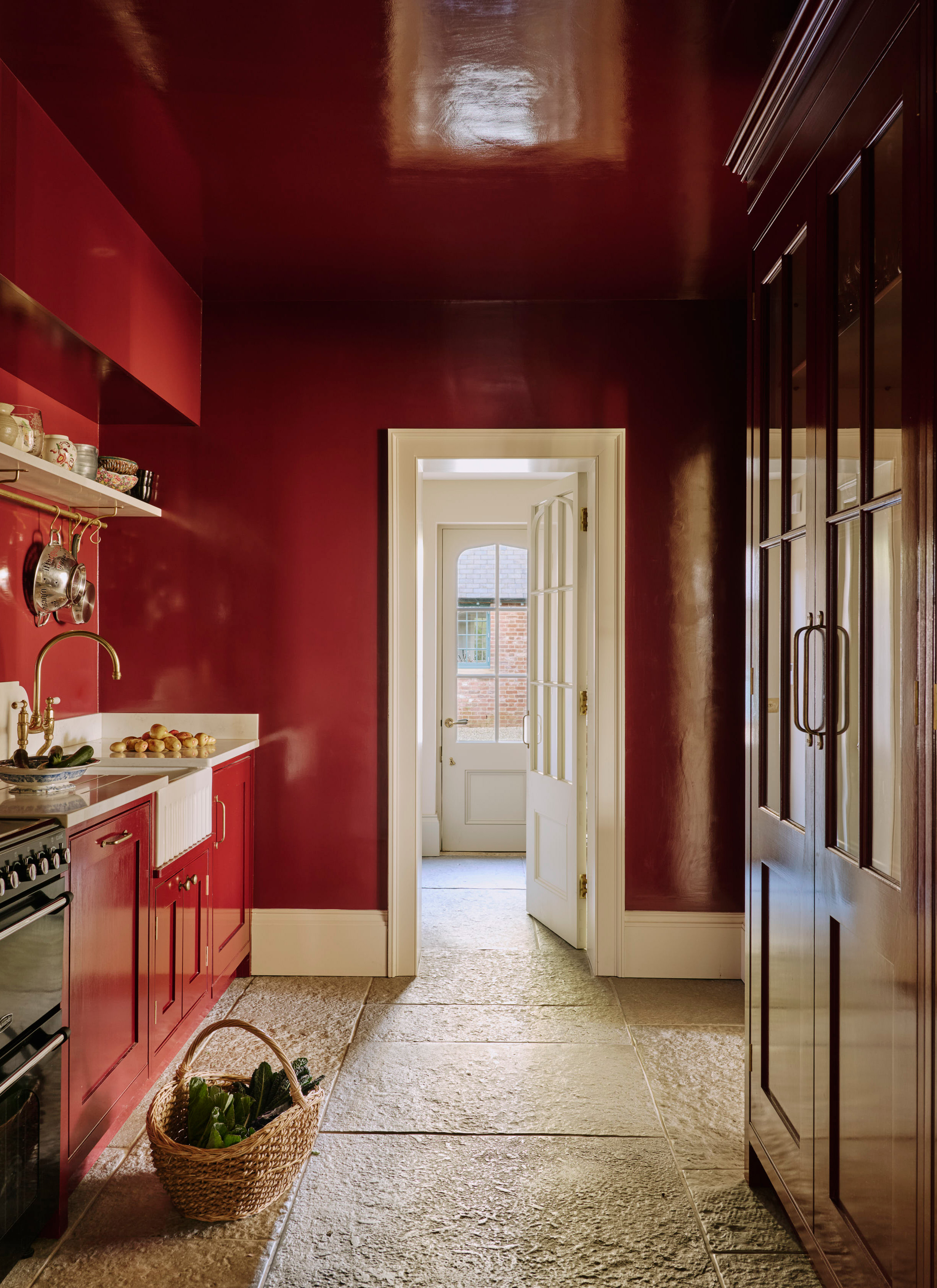 a narrow kitchen with red glossy walls and cabinets and a stone floor