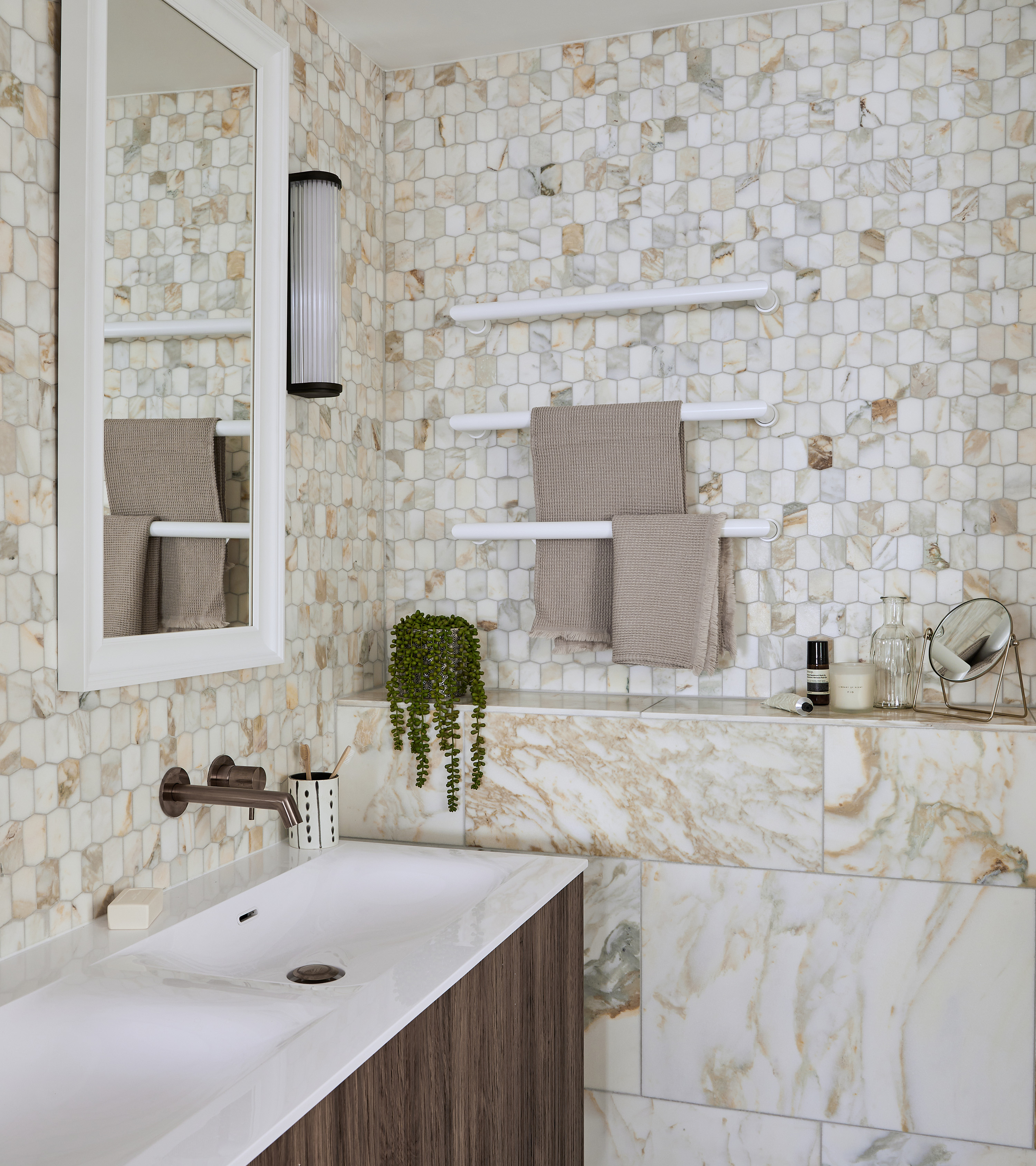 an all over beige marble bathroom with an arched recessed shelf, a dark wood vanity and a white towel tail on the wall