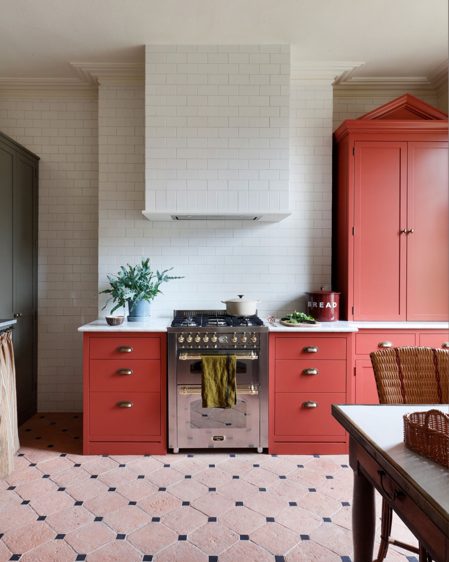 a kitchen with white tiles, birght red painted cabinets and a silver range cooker