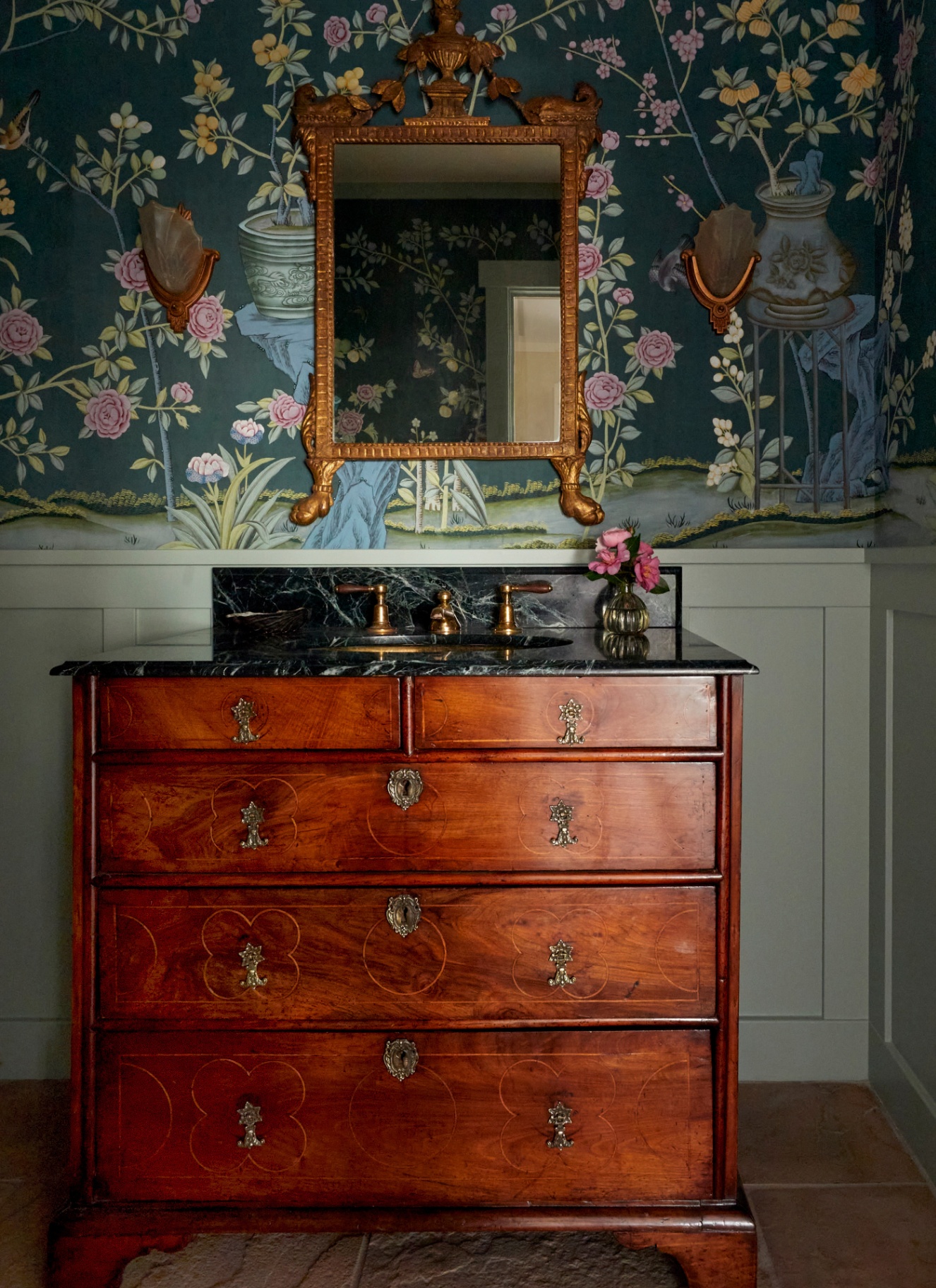 a bathroom with a dark floral wallpaper and a large antique vanity unit with a large gold ornate mirror above it