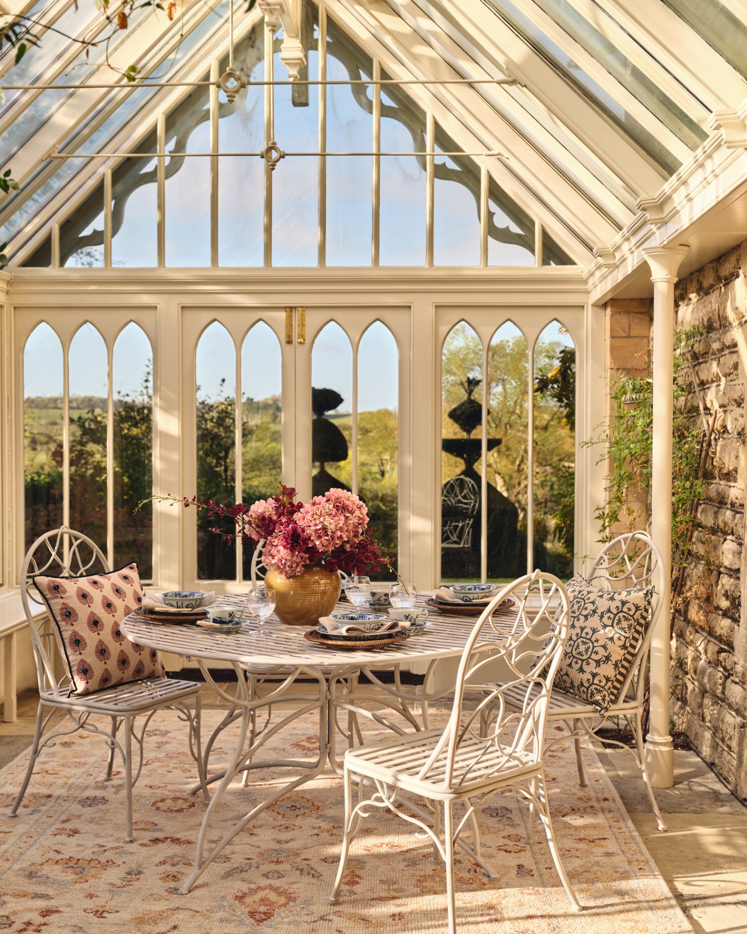a conservatory with cream ironwork and large windows, a cream patterned rub underneath a white bistro set
