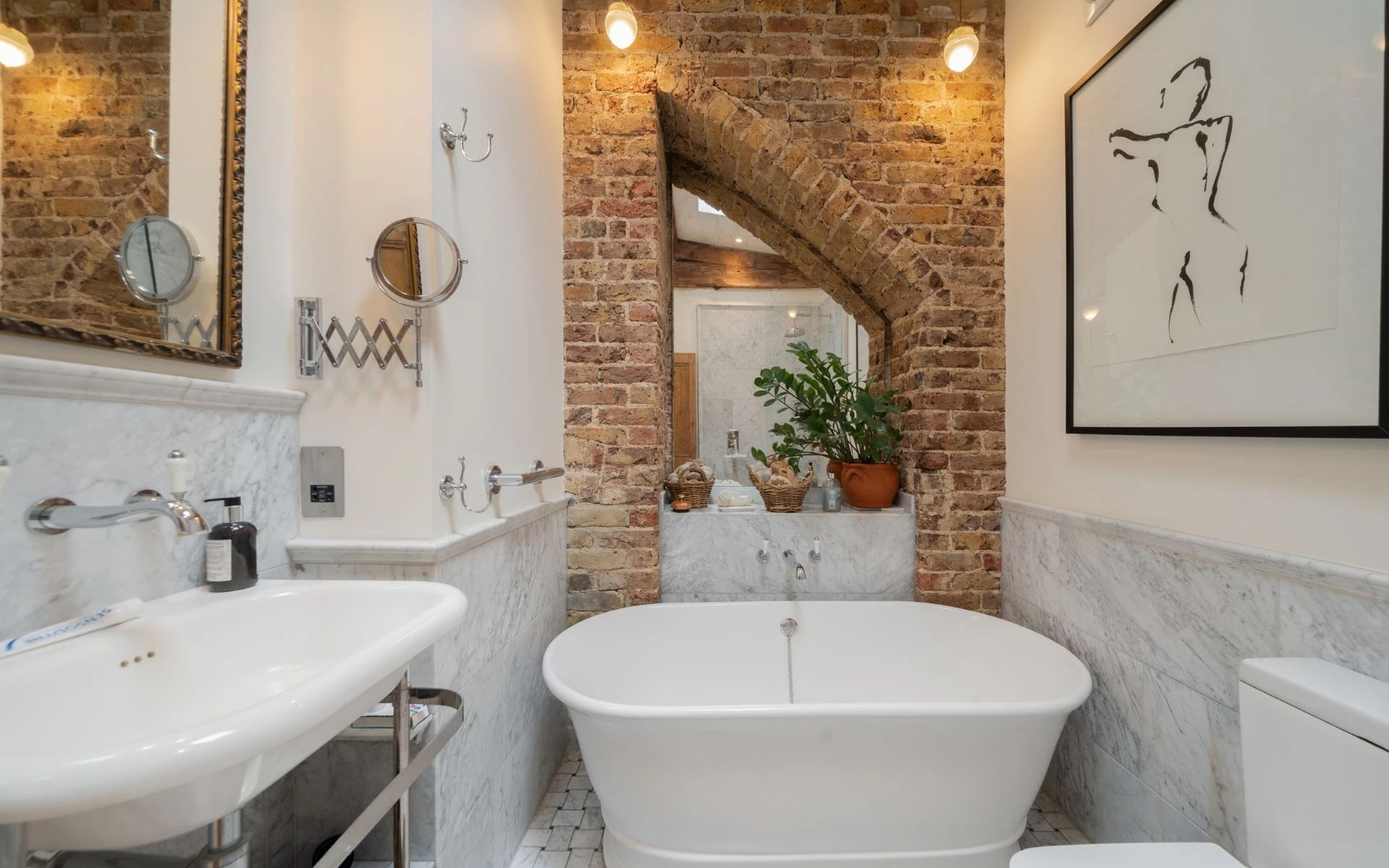 the bathroom of madonnas former london home with a freestanding white bath, exposed brick and a grey marble vanity