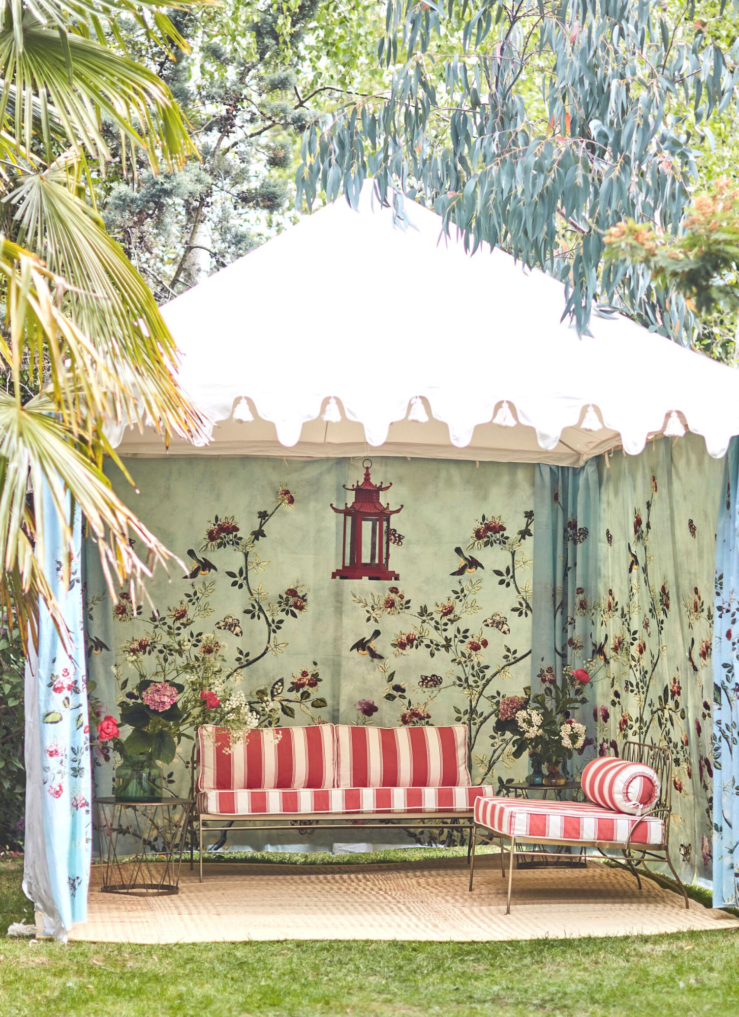 A FLORAL PRINT LARGE GAZEBO WITH A SOFA AND CHAIR UNDERNEATH WITH WHITE AND RED SEAT CUSHIONS
