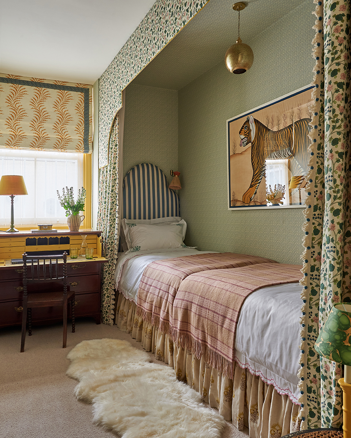 a bedroom with a single bed built in nook, a print of a tiger above it, a sheep skin rug and a vintage dressing table and chair in front of a window