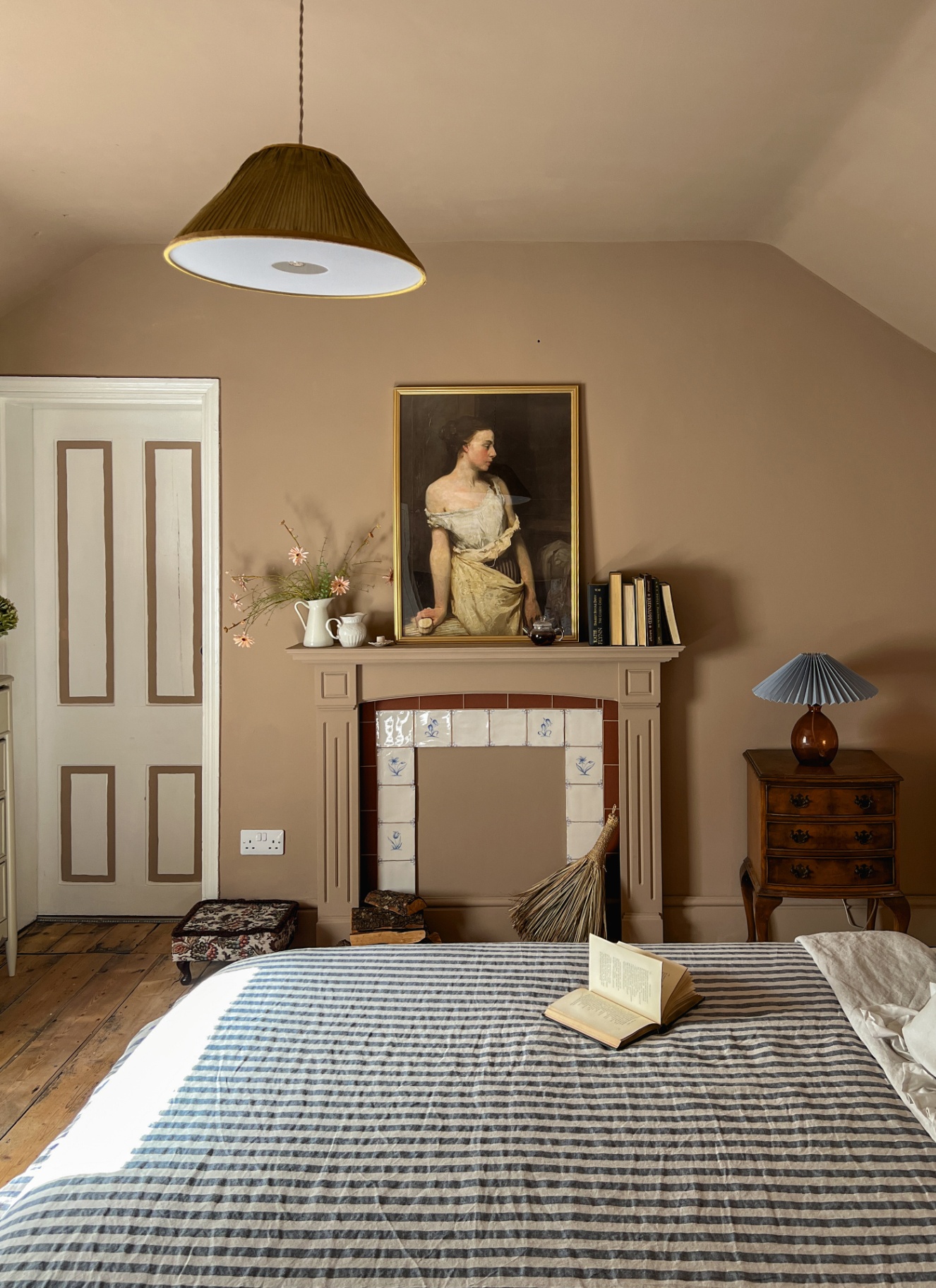 a bedroom with brown walls, a fireplace with delft tiles and a bed with stripe bedding