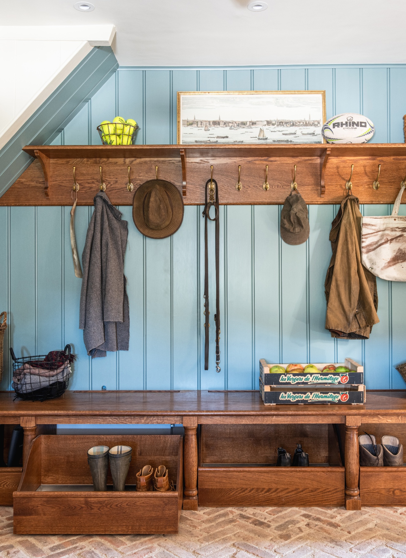 a boot room with blue panelled walls, dark wood joinery with drawers filled with shoes and hooks with hats, coats and dog leads