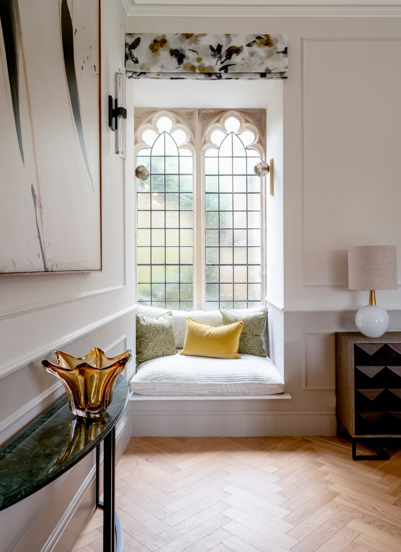 a landing hall way with an old arched window with a window seat and wooden parquet flooring
