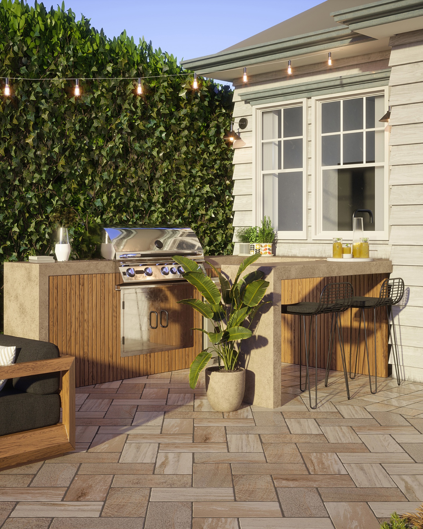 an outdoor kitchen area with festoon lights overhead, a grey breakfast bar with two black metal chairs and a bbq and kitchen area behind it