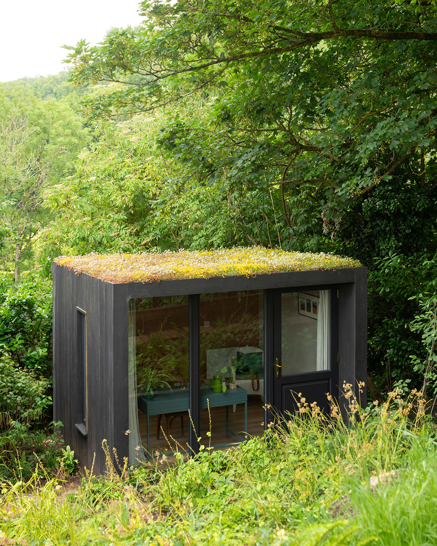 a black garden room with grass on the roof surrounded by grass and green trees