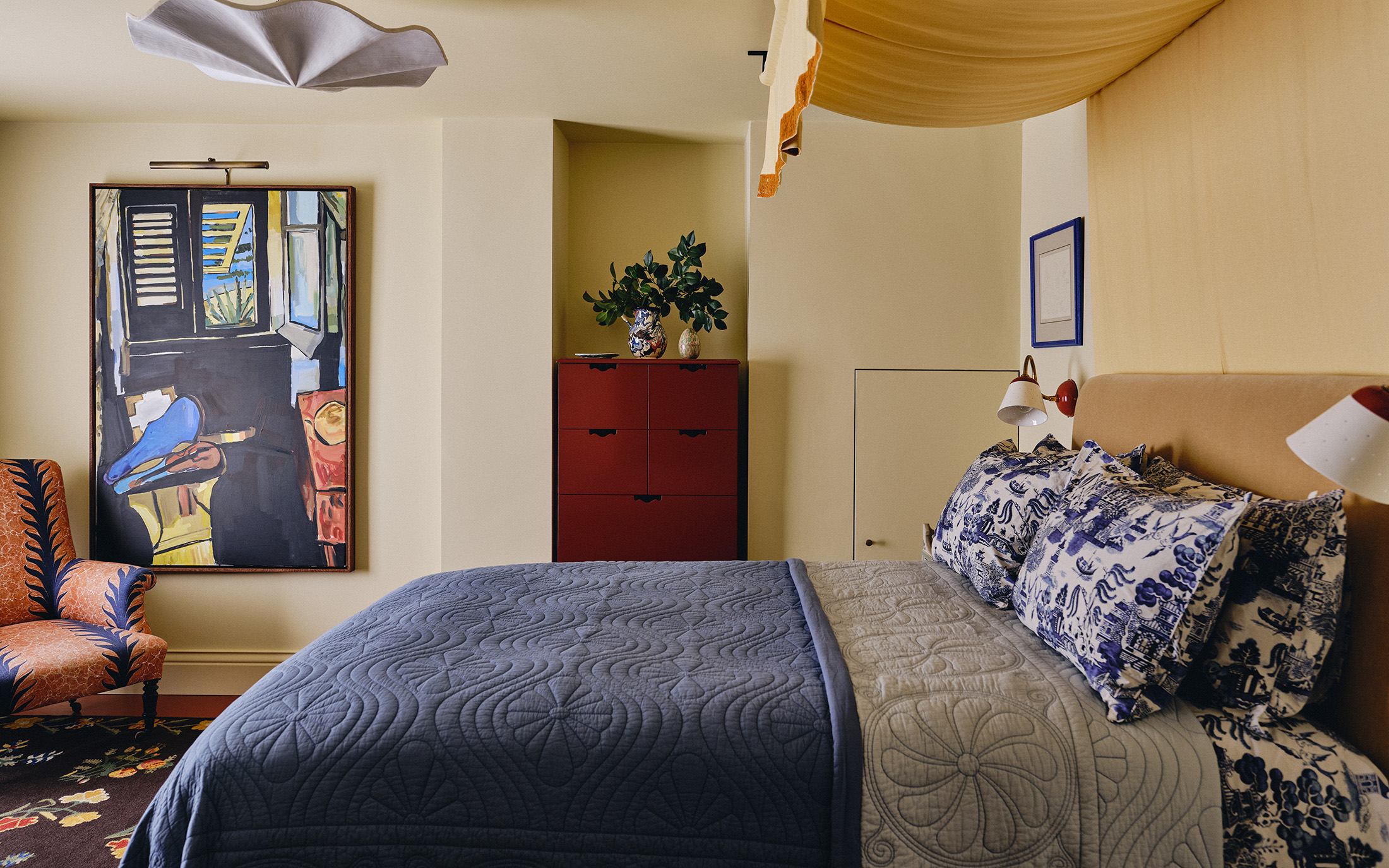a pale yellow bedroom with a double bed and a dark blue bed spread