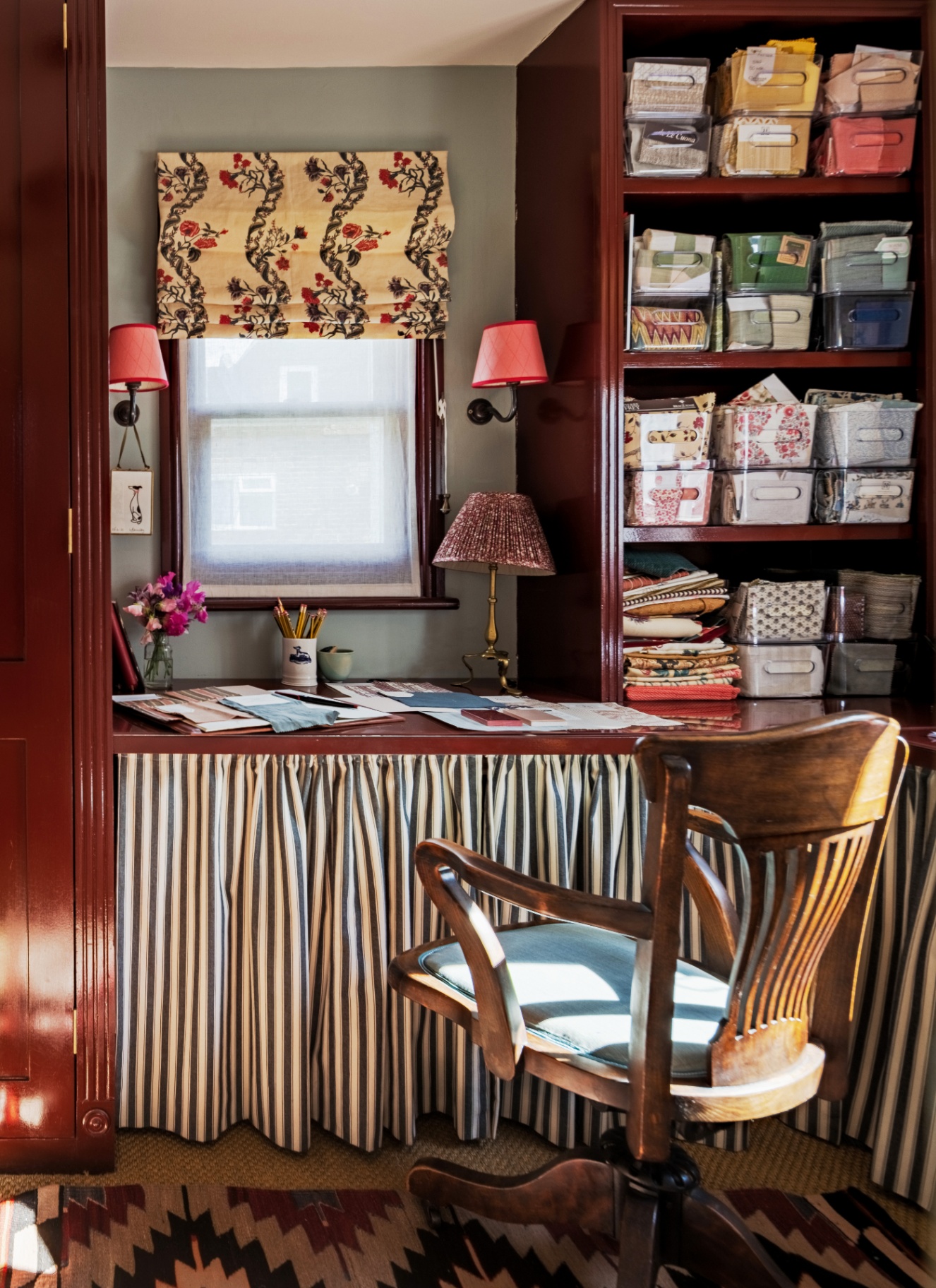 Small built-in desk nook in a deep gloss cherry-red alcove, featuring a classic black and white striped fabric skirt concealing storage beneath the counter