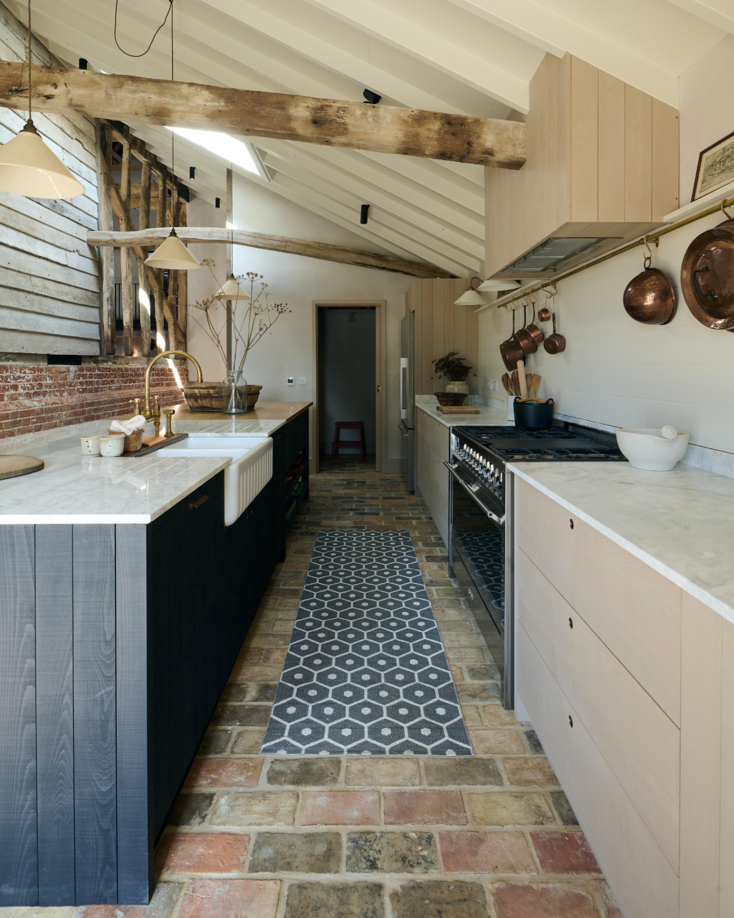 a kitchen with stone flooring an a navy and white patterned runner, cream and navy kitchen cabinets with marble tops and wooden beams on the ceiling