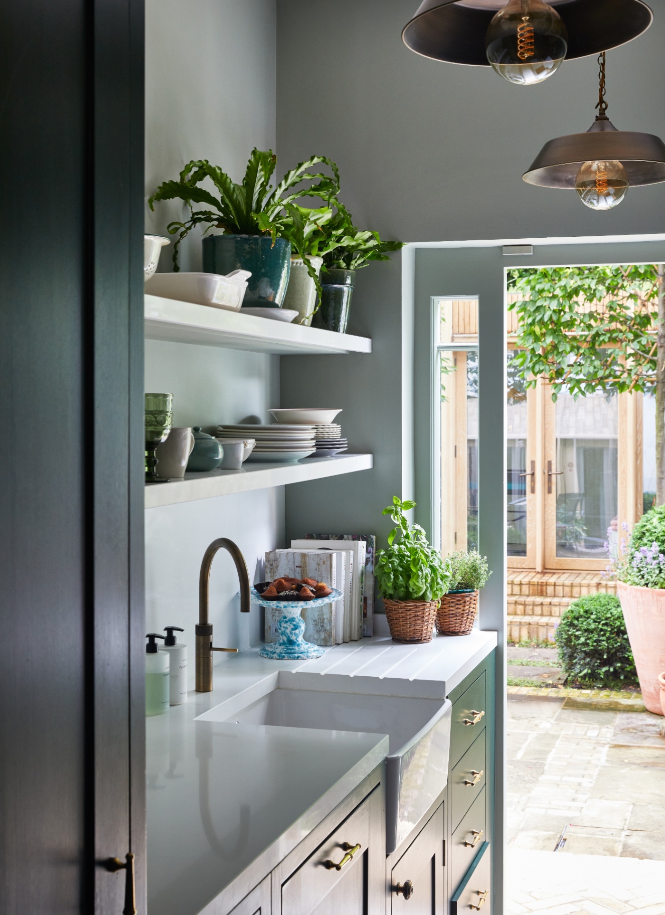 a narrow kitchen with navy cabinetry, open shelves with plates and bowls and an open door looking out to a patio garden