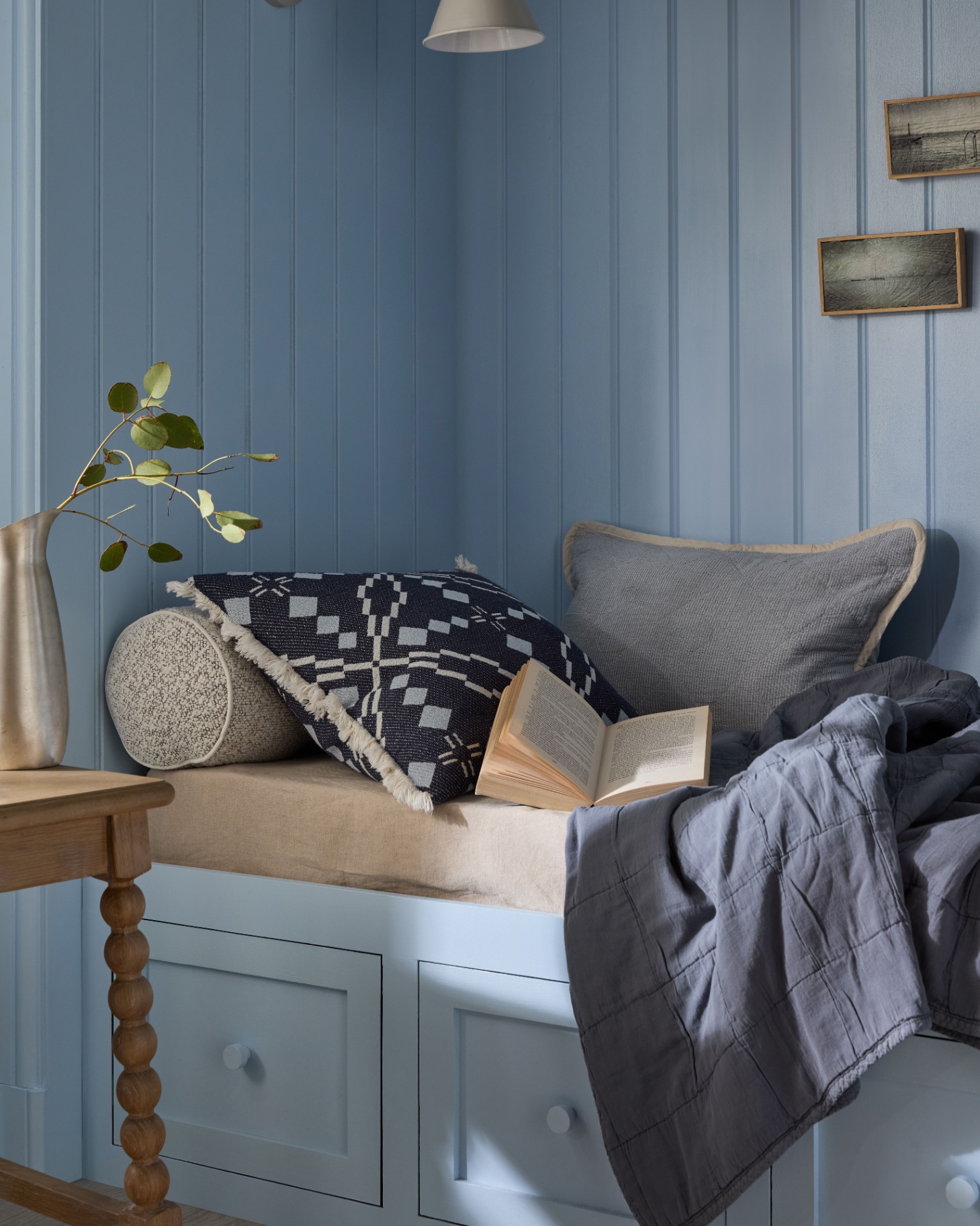 a reading nook with a sky blue paneled wall, a day bed with drawers underneath and a dark blue cushion and throw on top