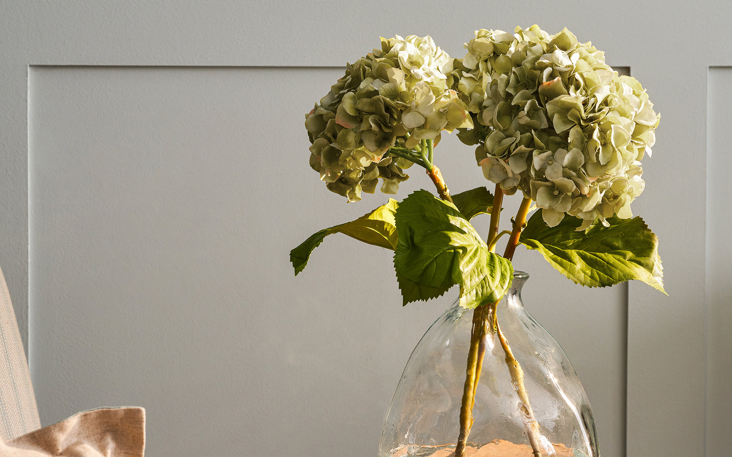 three green faux hydrangea stems in a clear glass vase