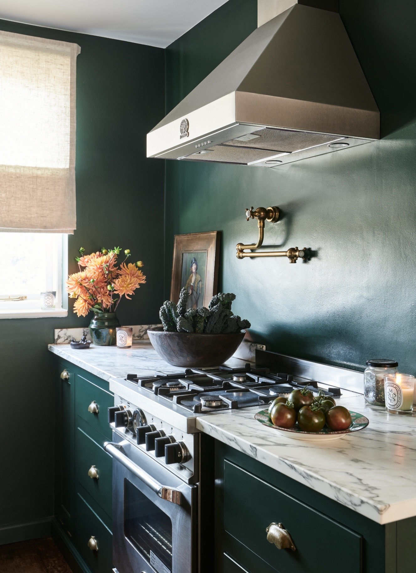 A kitchen with dark green walls and cabinetry, a white marble countertop and a silver oven and hood