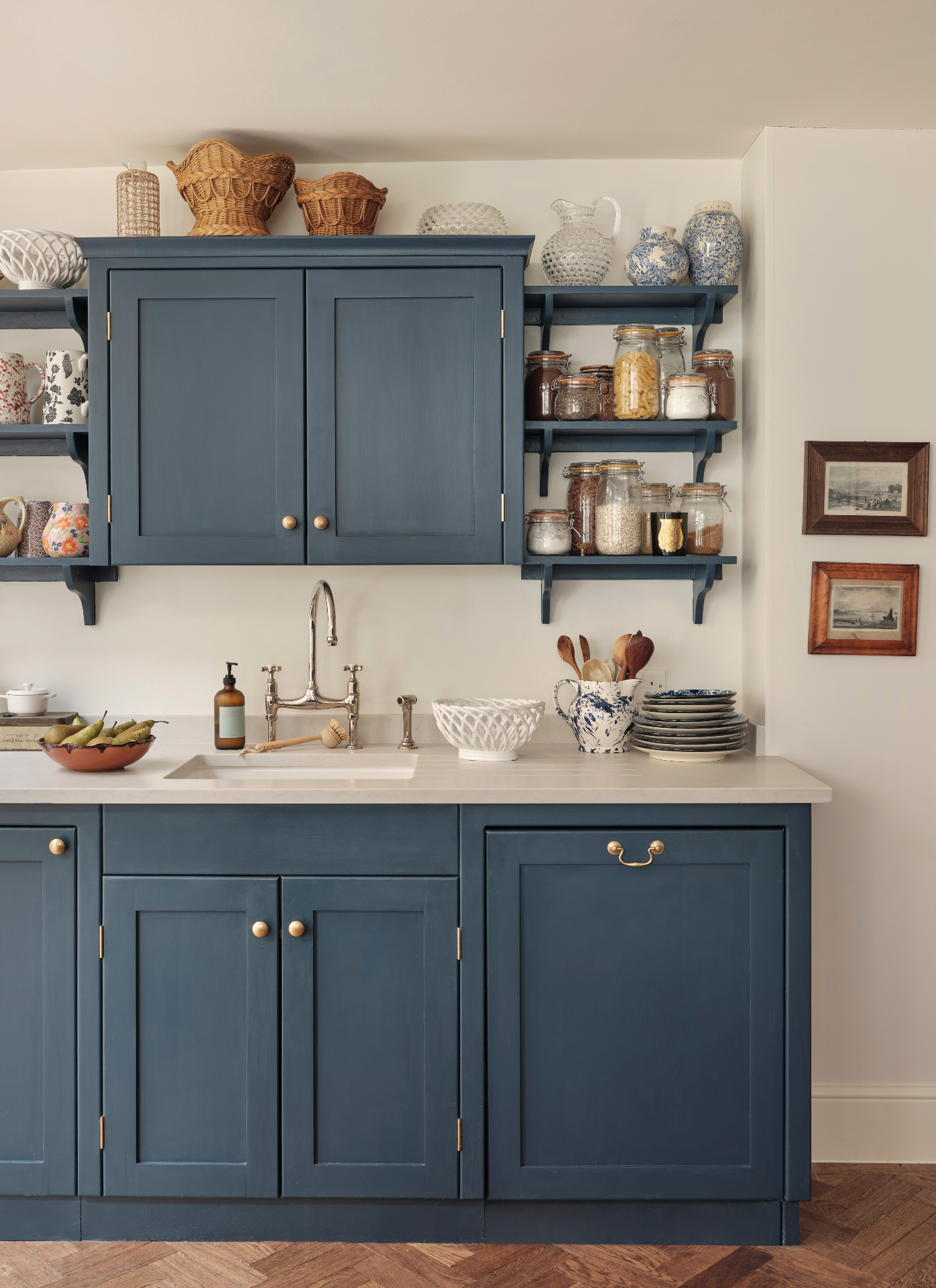 a kitchen sink area with blue cabinets, a blue wall cupboard and blue shelves either side of the cupboard filled with jars of food